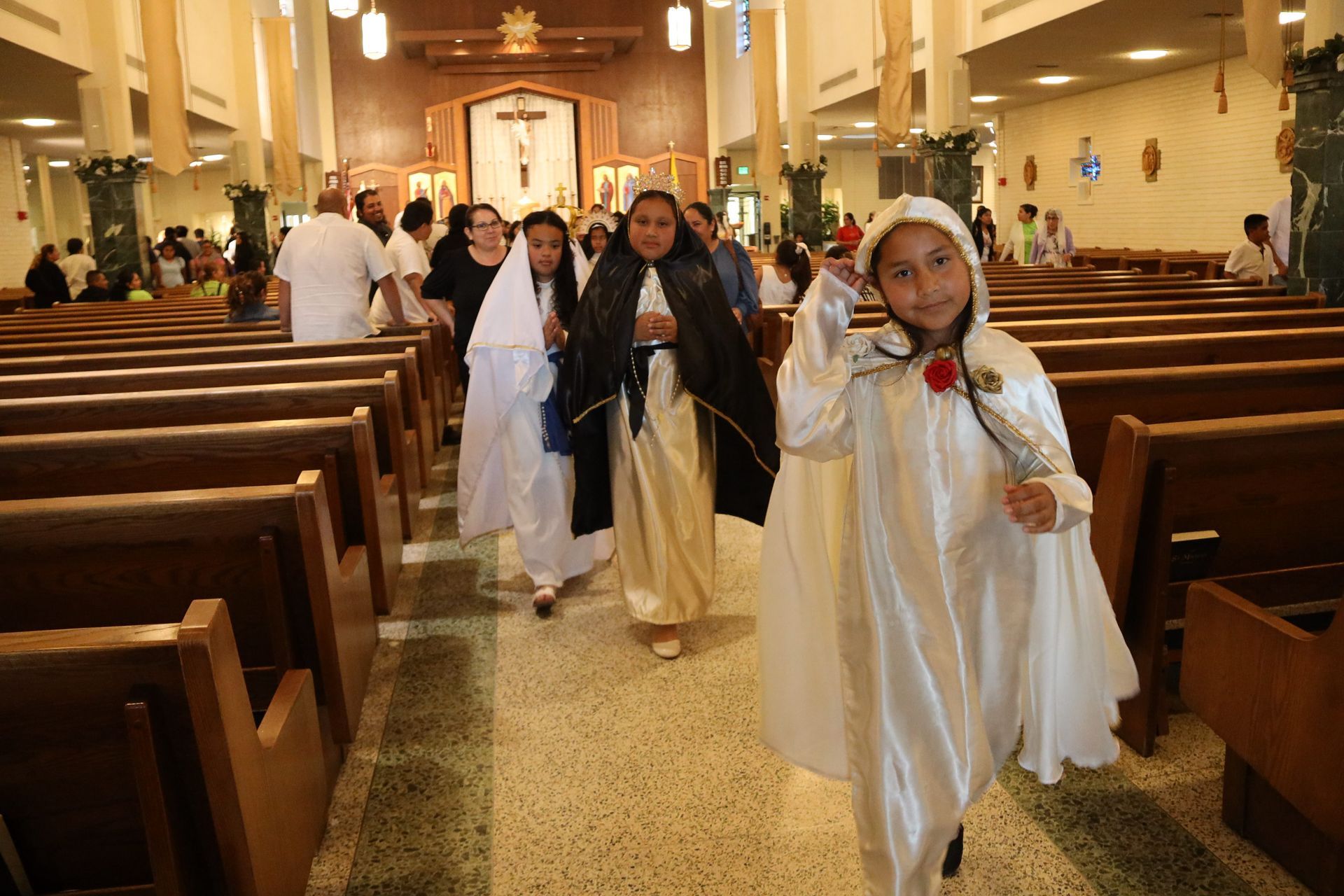 Children in white robes walking down church aisle during a religious procession