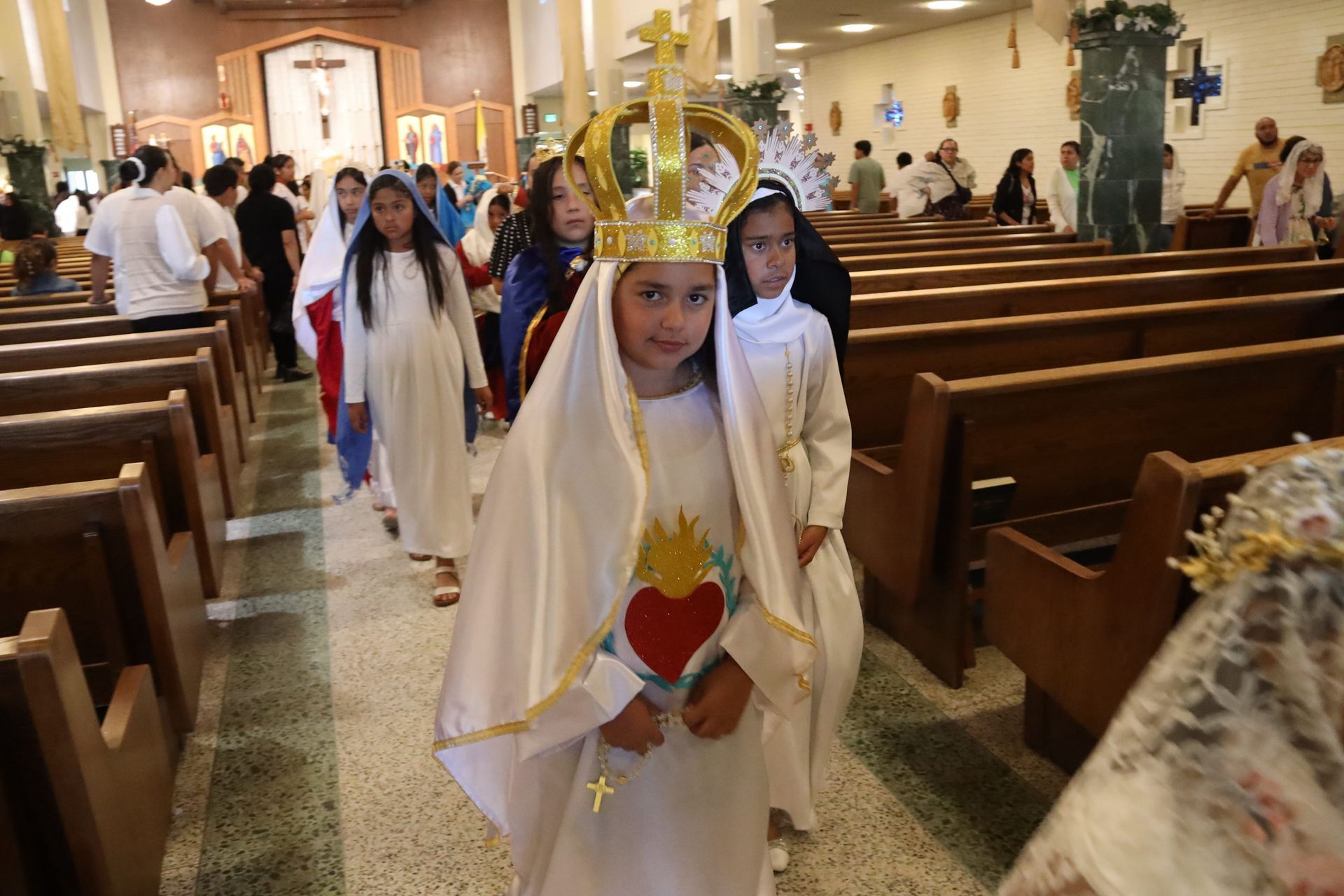 Children in white robes process through a church aisle during a religious ceremony