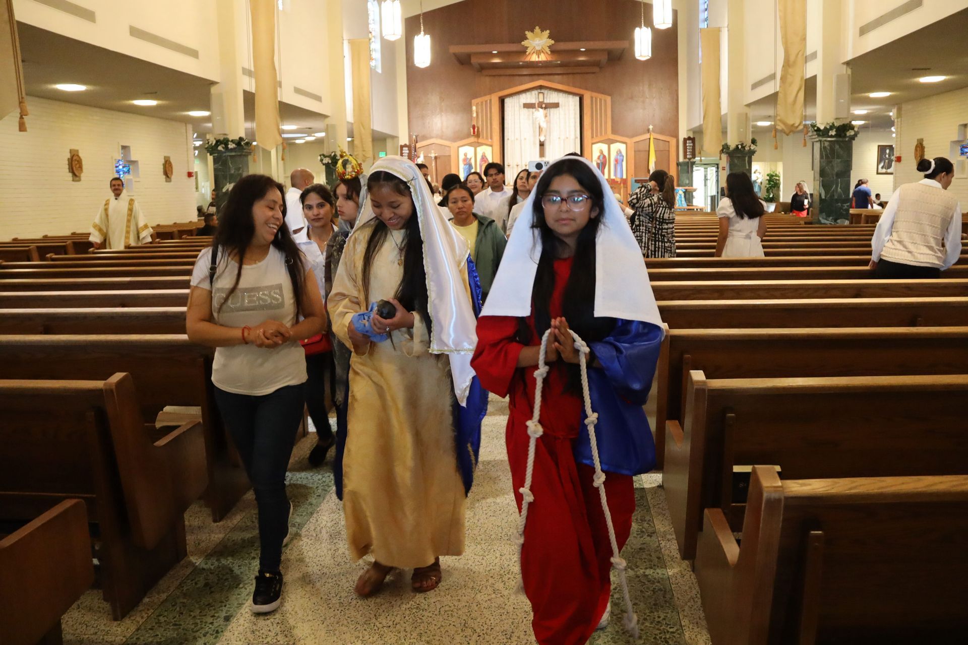 Three women in costume walking down a church aisle during a ceremony