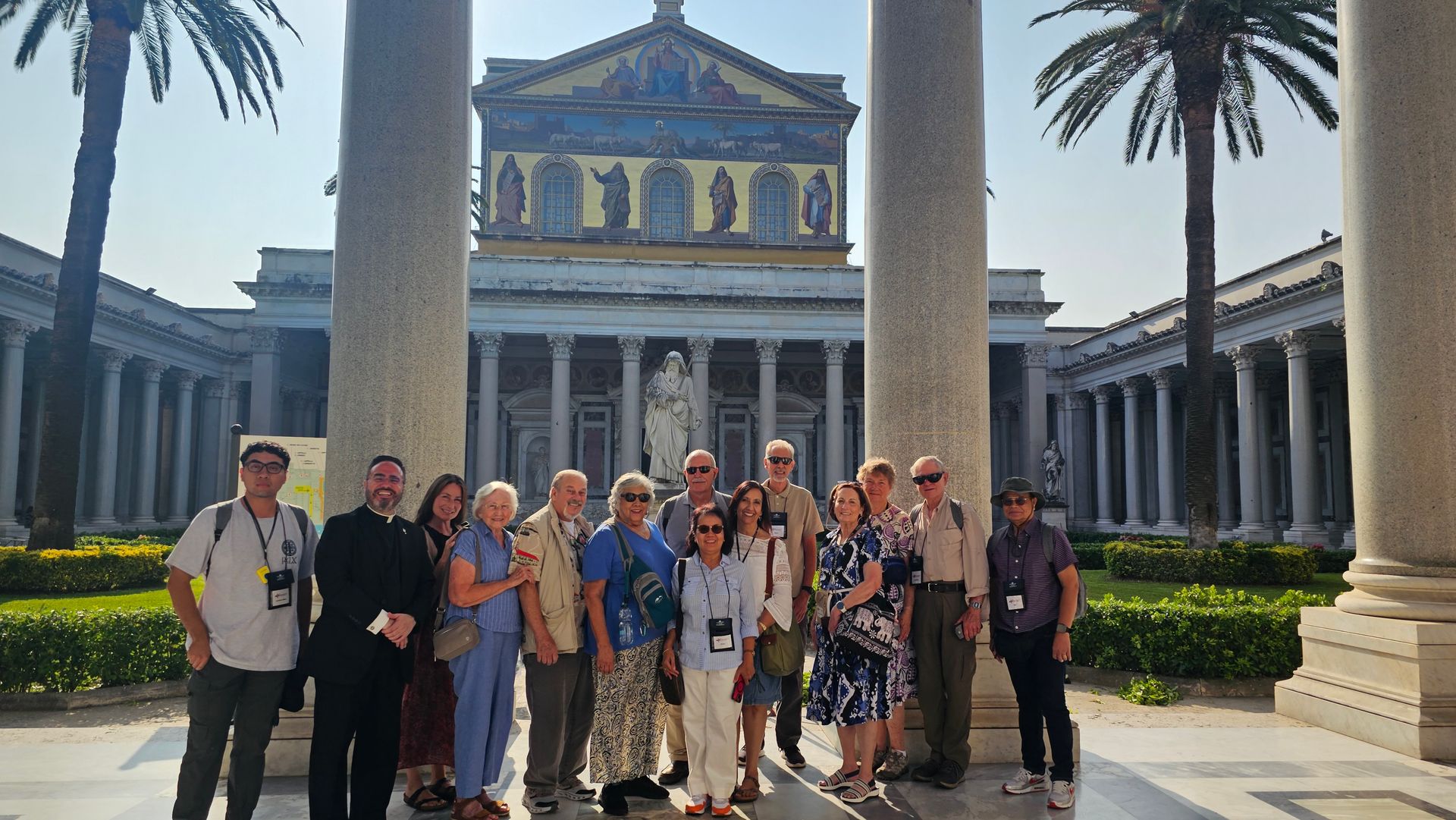 Group posing in front of a grand historic building with columns and palm trees, in bright sunlight.
