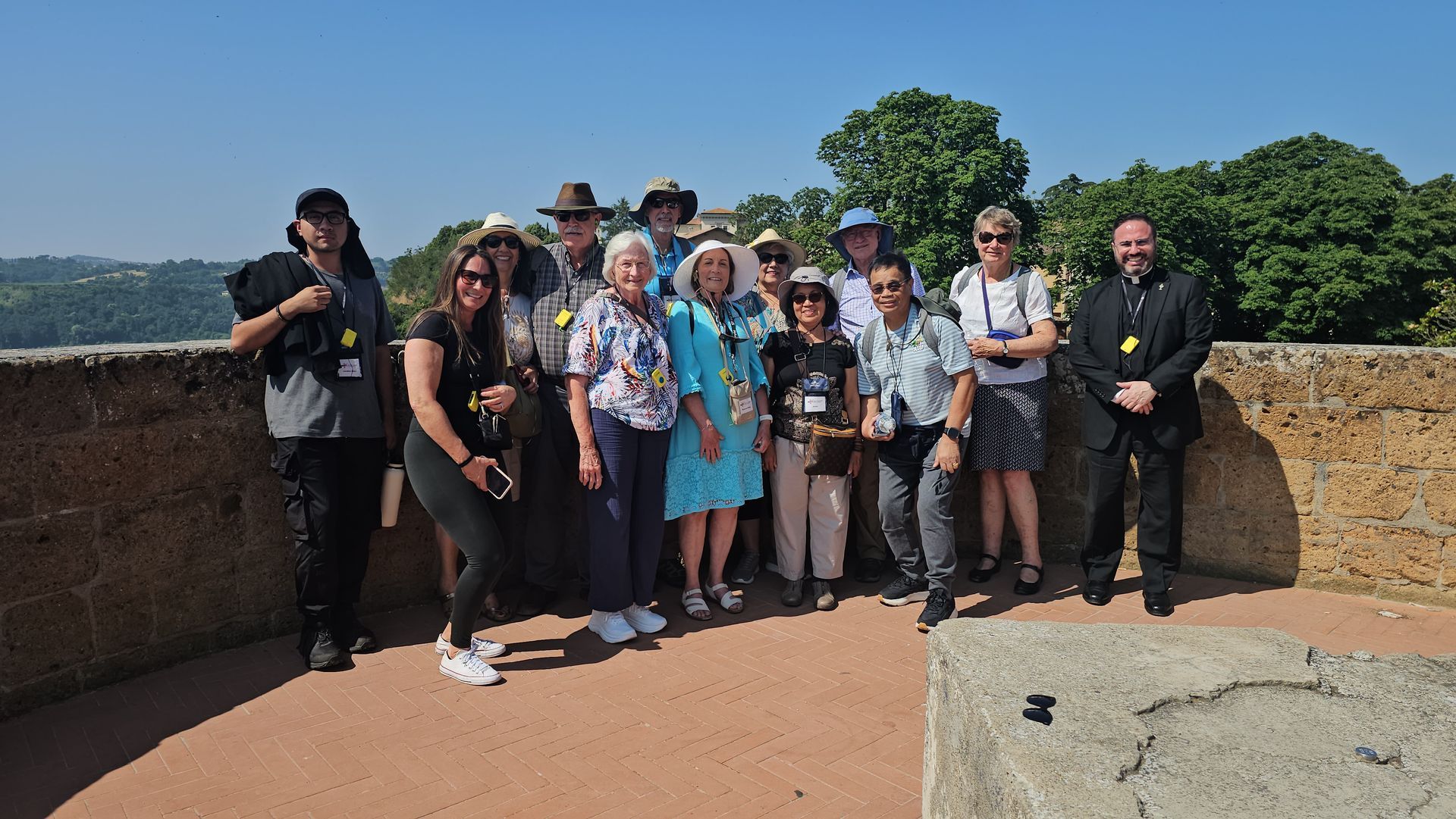 Group of people posing on a stone overlook with trees in the background, smiling in bright daylight