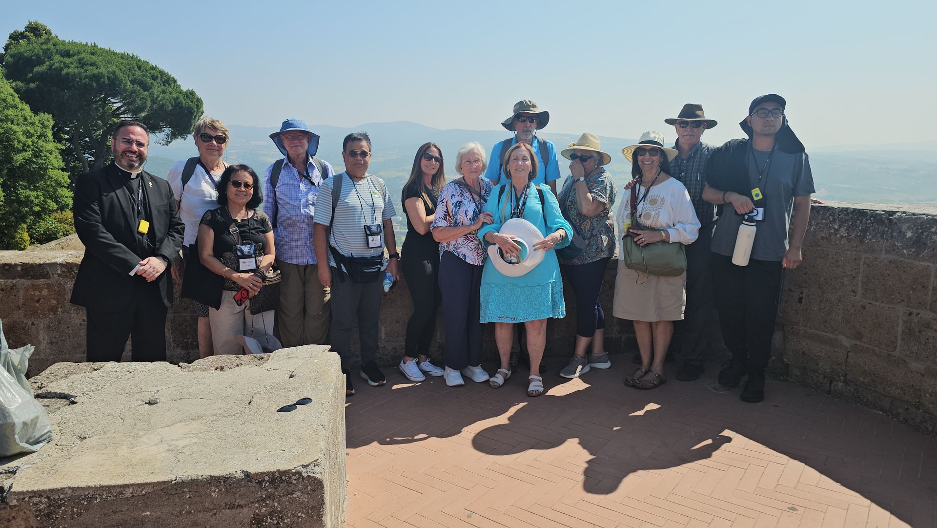 Group of people posing outdoors at a scenic overlook on a sunny day, with ocean and sky in the background.