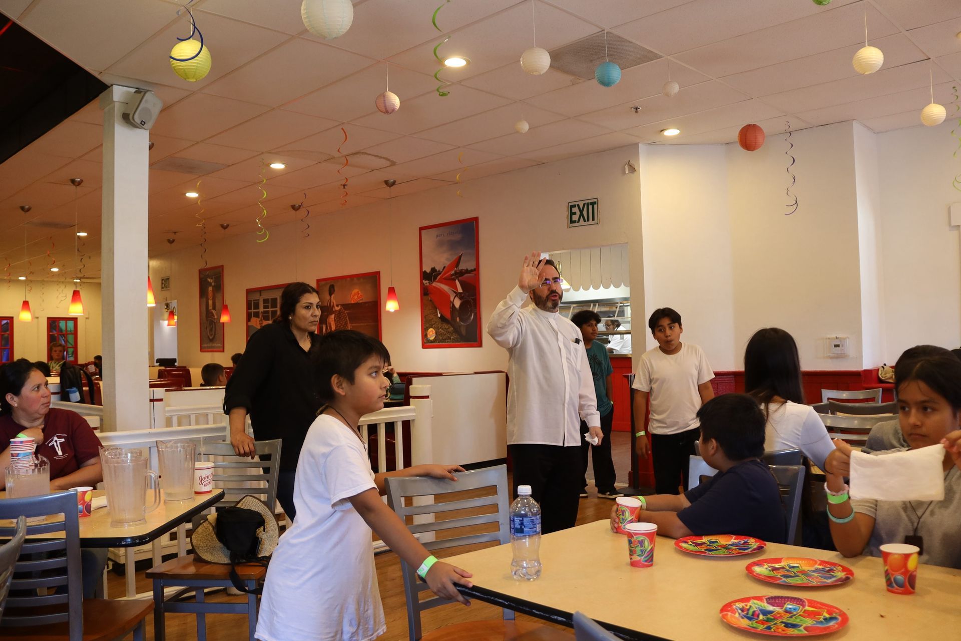 People gathered around tables in a bright cafe or dining hall with hanging lights and colorful wall decor