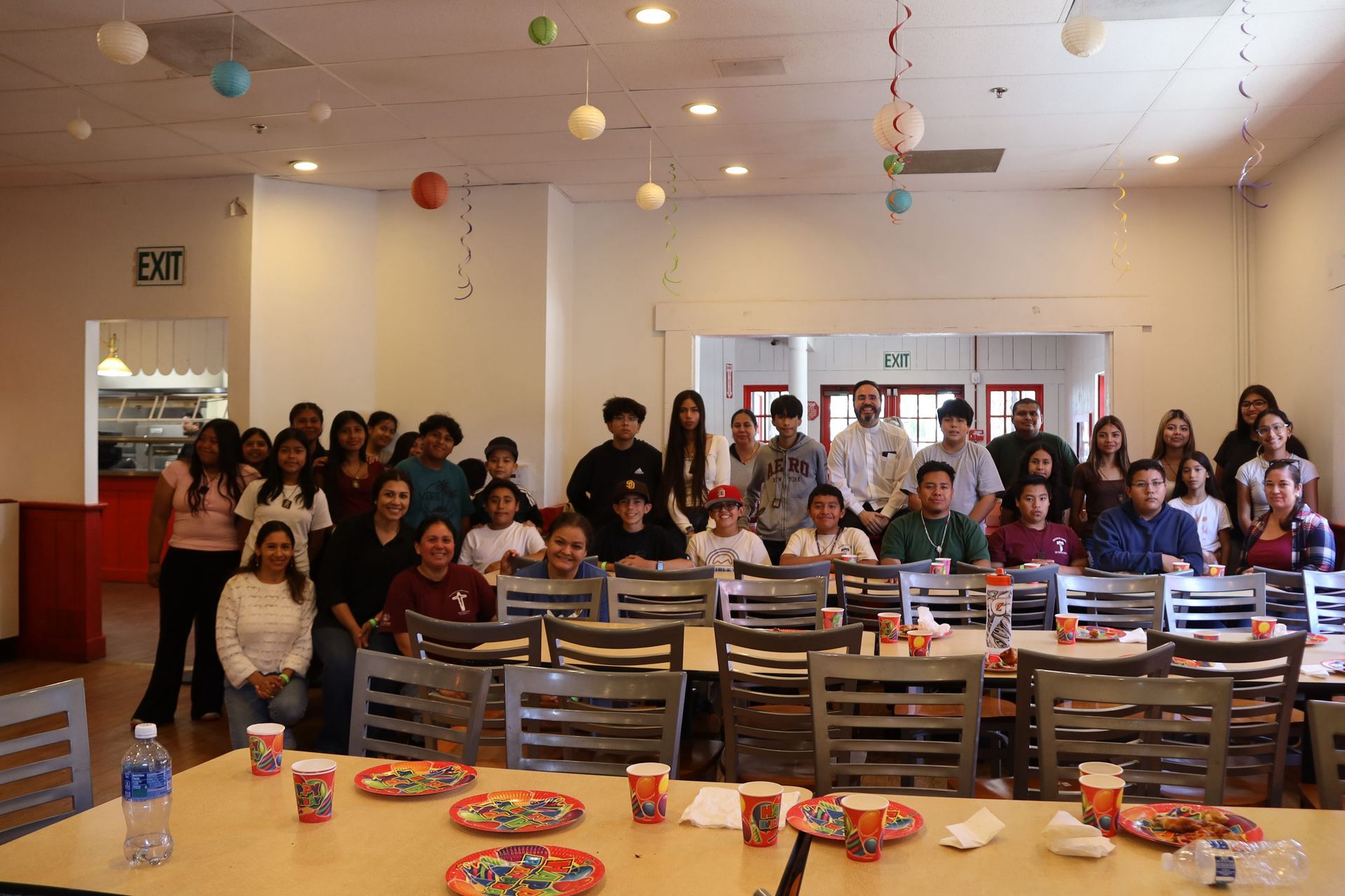 Group seated in a cafeteria with tables of snacks and colorful hanging decorations