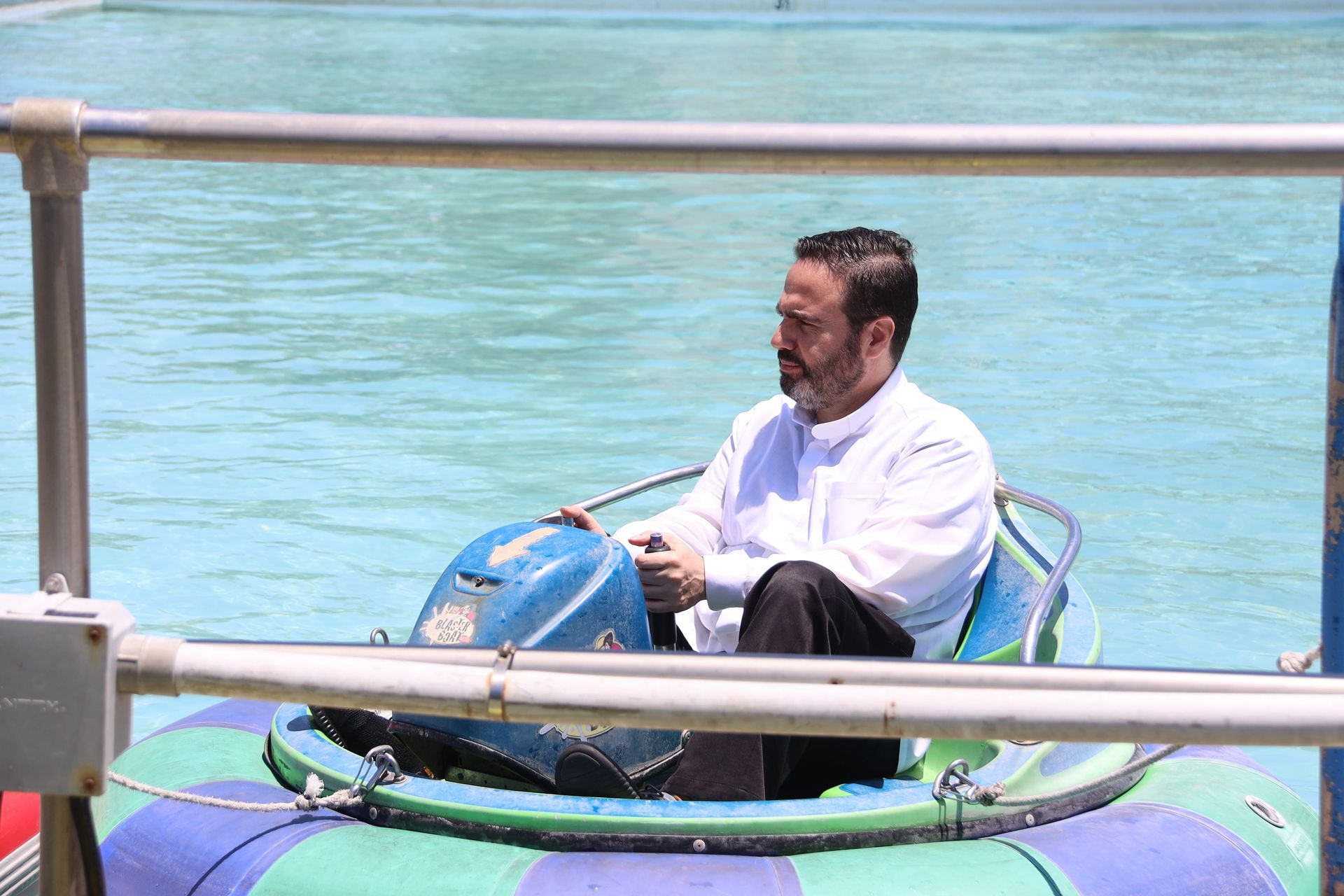 Man in white shirt riding a small blue-green boat on clear water, holding a blue globe-shaped object