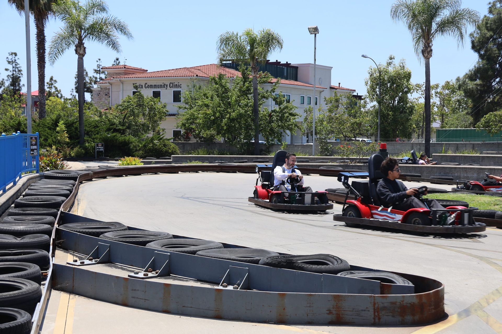 Go-kart racers turning on an outdoor track beside stacked tires and palm trees