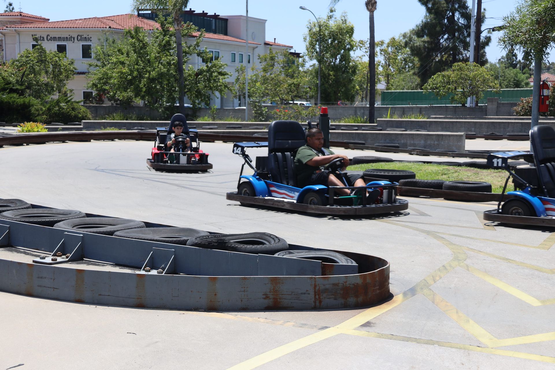 People driving go-karts on an outdoor track with concrete barriers on a sunny day