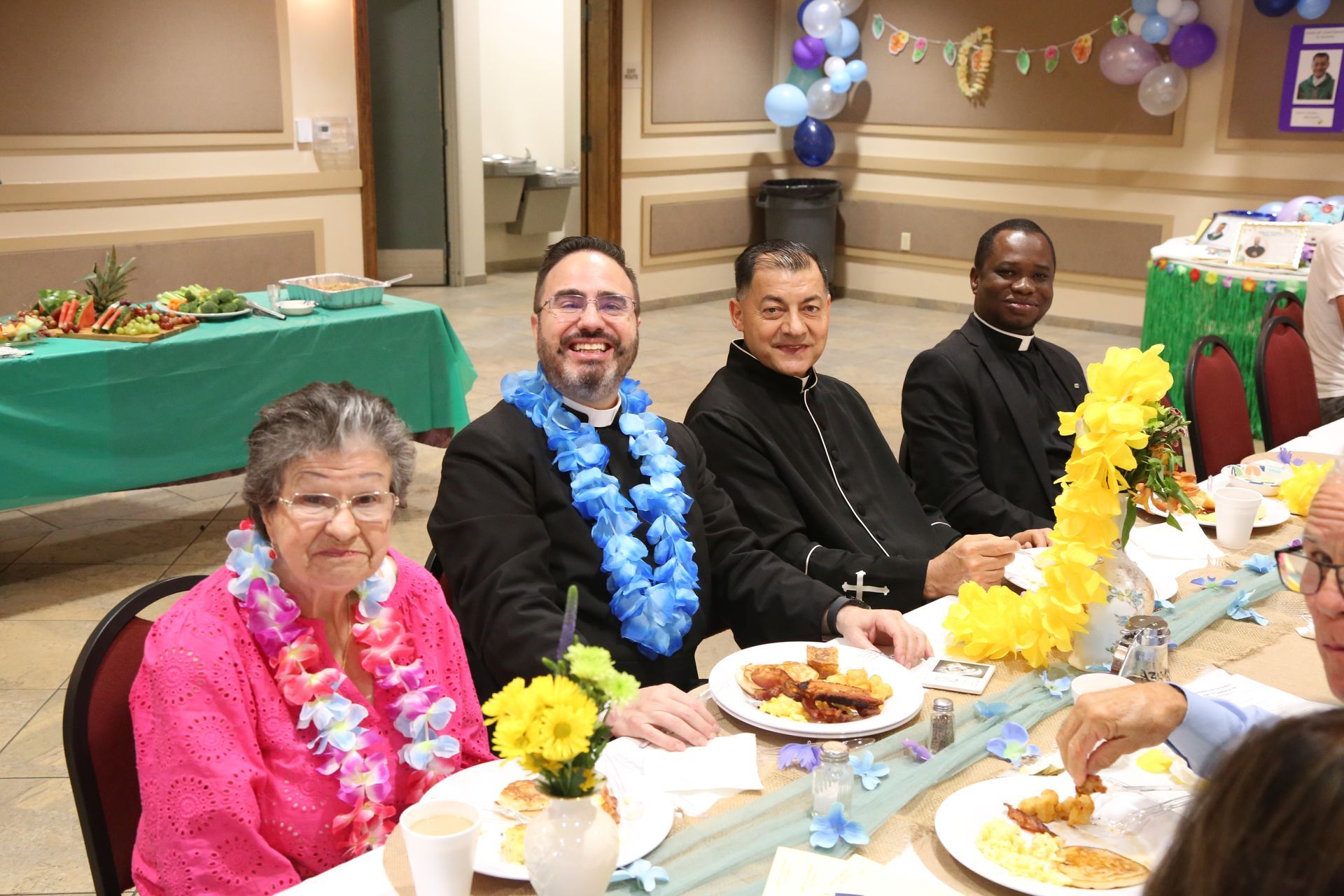 People seated at a decorated banquet table with flowers and plates, smiling during a celebration