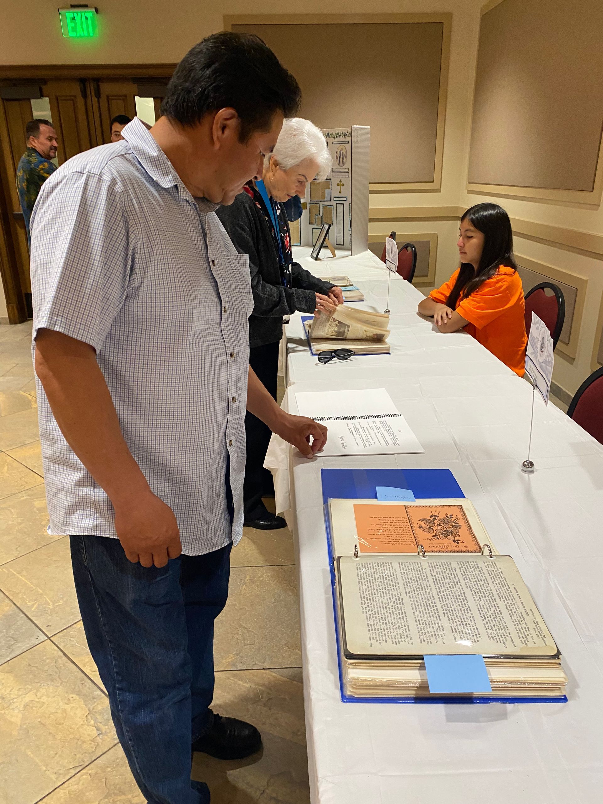 Man viewing books at a table display while a woman sits behind the table in a conference room