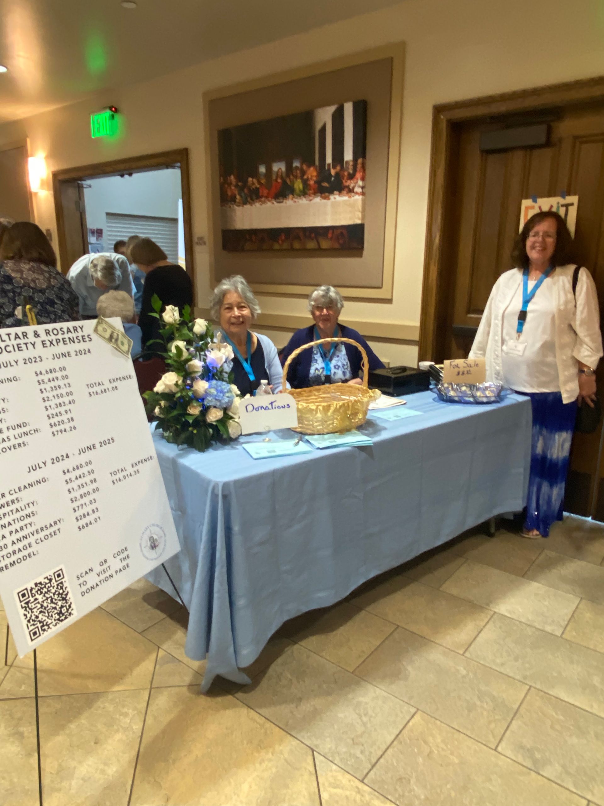 Hospital event table with volunteers, a basket, flowers, and a sign in a hallway