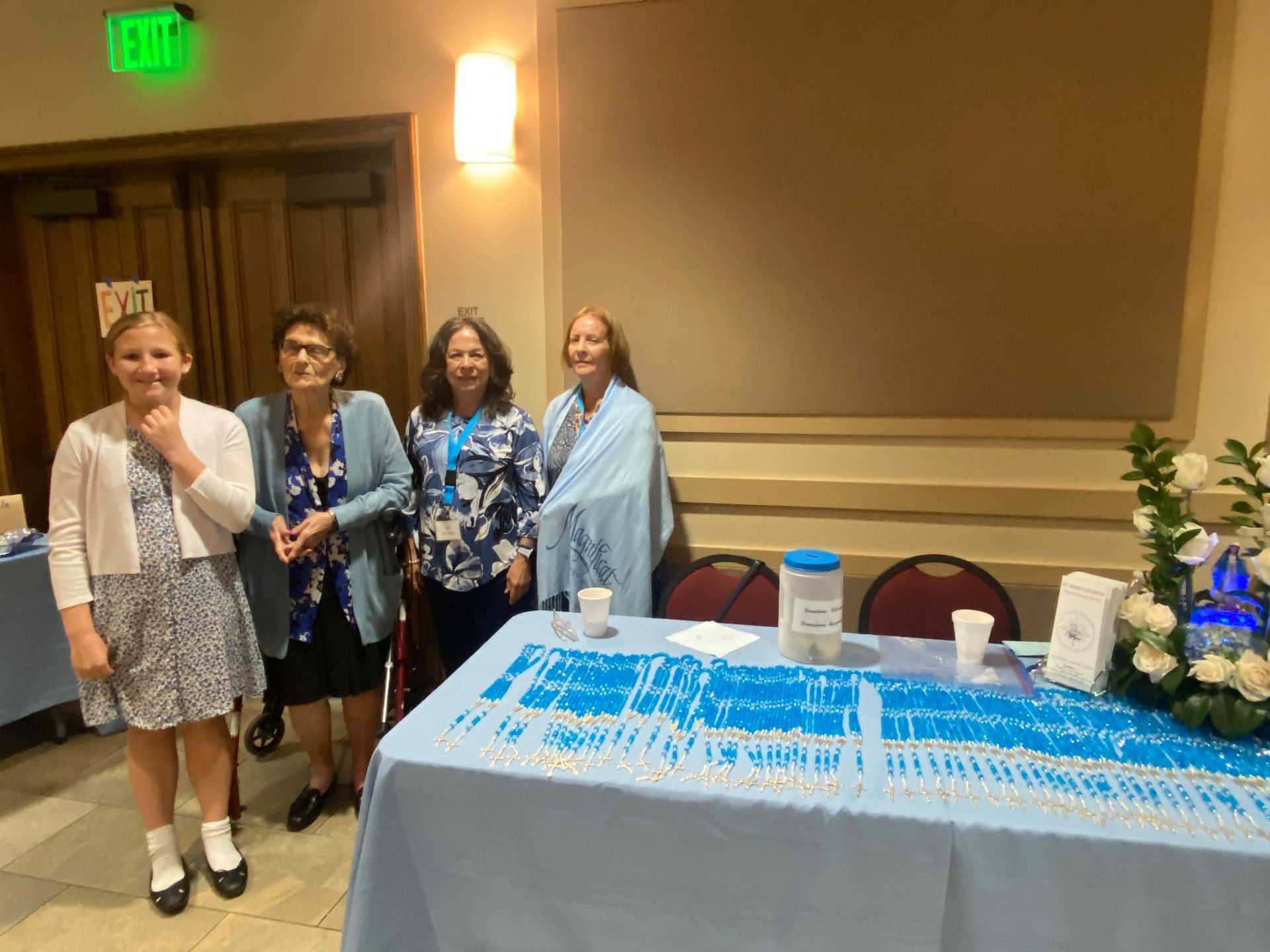 Four women stand beside a blue-and-white table display at an indoor event.