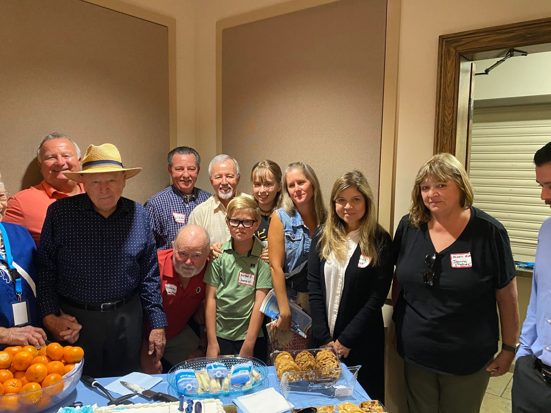 Group of people standing behind a table with oranges and packaged snacks in a room