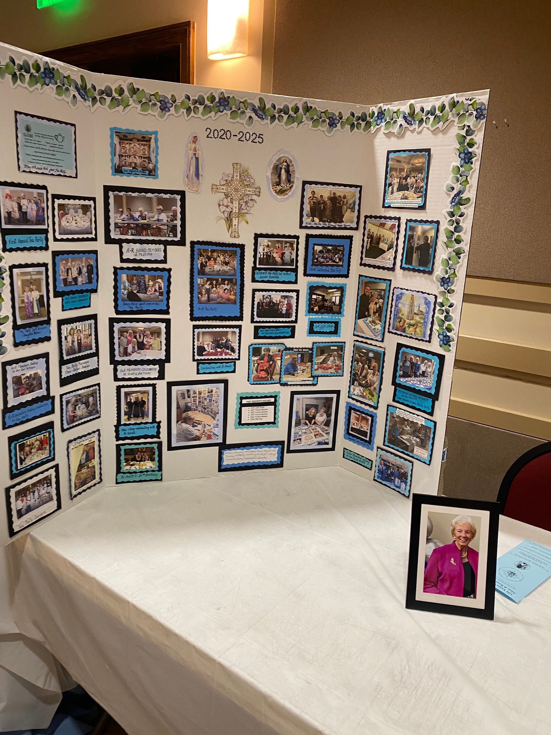 Photo display board covered with many small framed snapshots on a white table at an event.