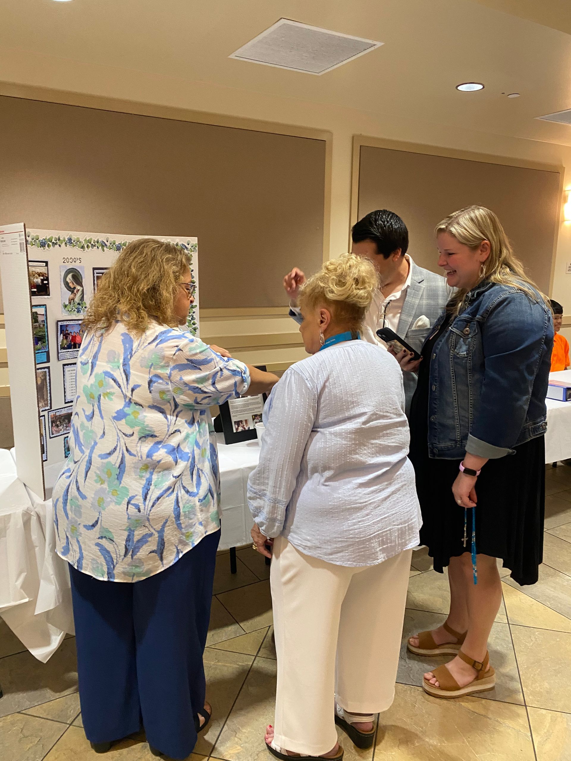 Four people discussing items on a display board in a conference room, with photos and notes visible.