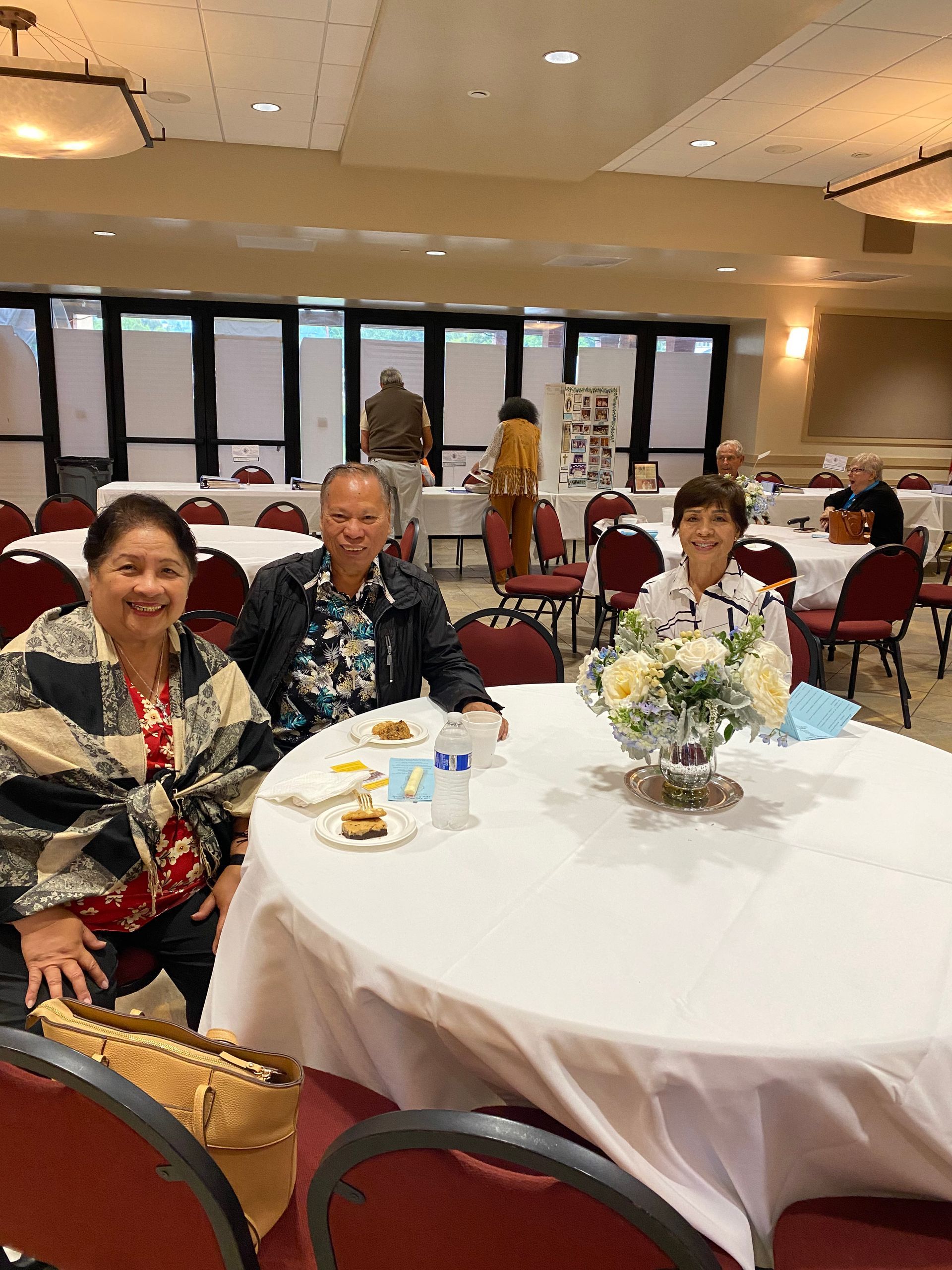 People seated at round banquet tables in a bright event hall with floral centerpieces
