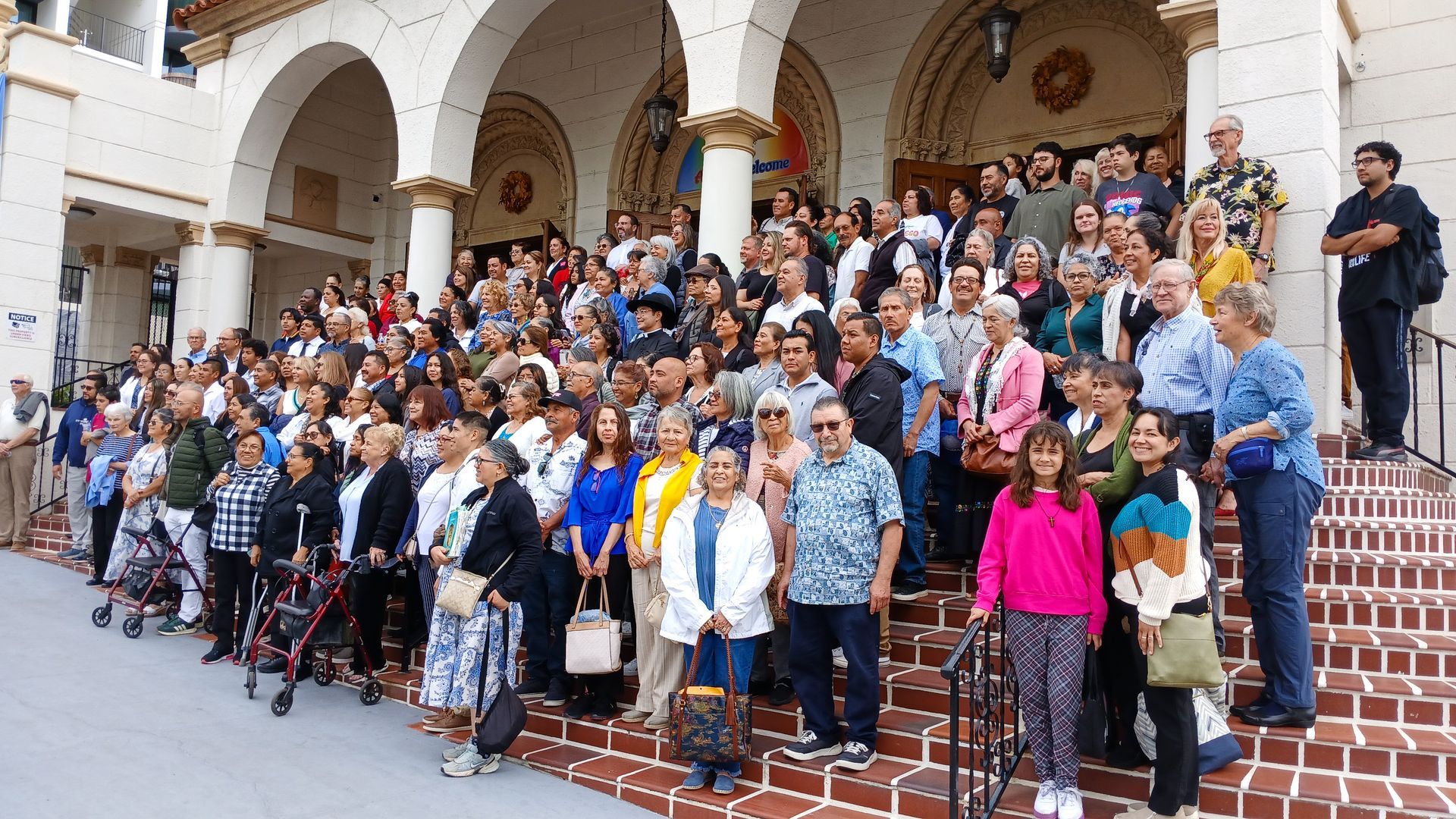 Large group posing on the steps of a white stone building with arches and brick stairs.