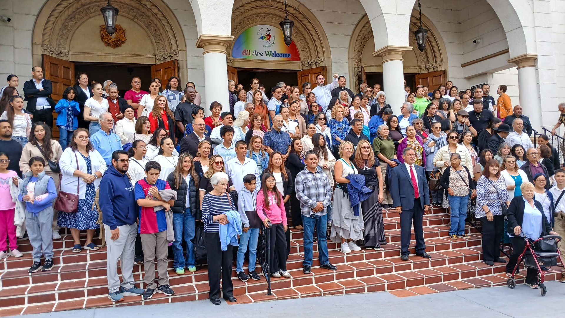 Large group gathered on church steps, posing for a photo in front of arched entrance.