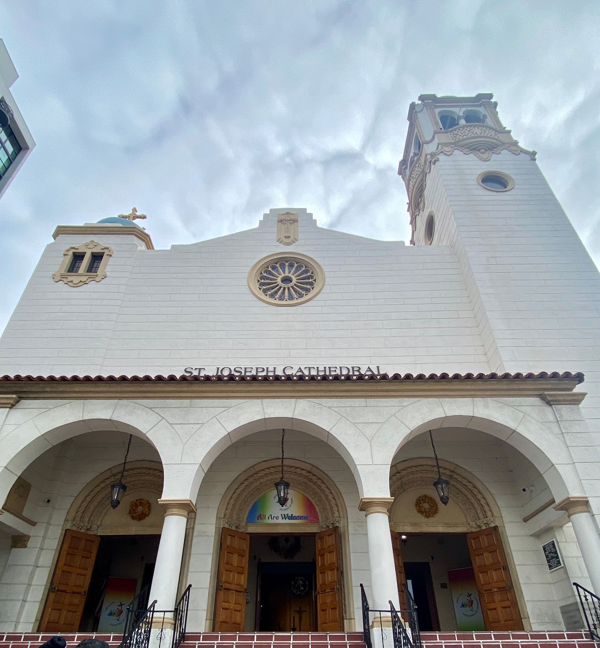 White church facade with arches and a tall bell tower against a cloudy sky