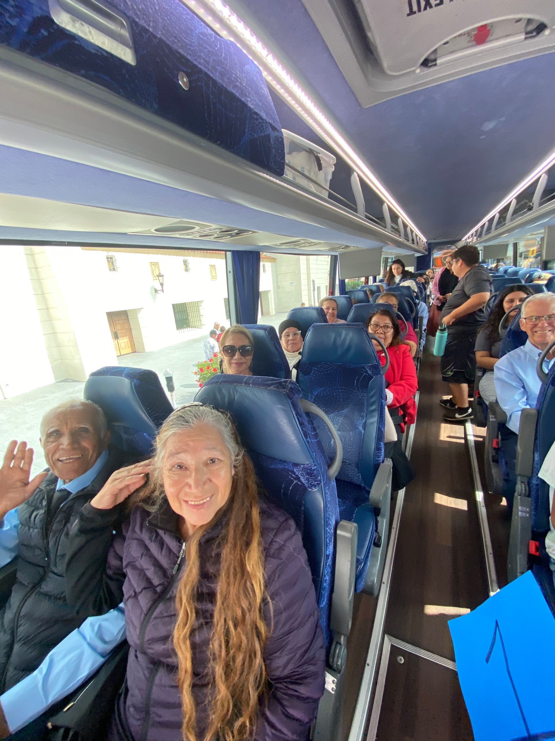 Passengers seated inside a tour bus, smiling and waving down the aisle.