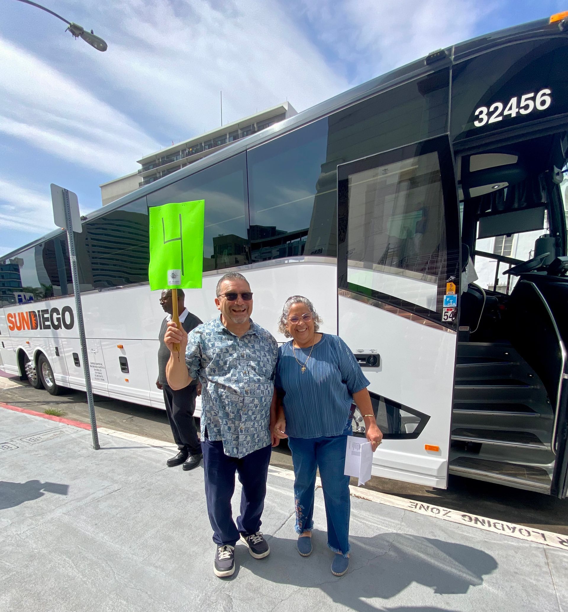 Two people posing beside a white tour bus, one holding a bright green sign with a number 4.