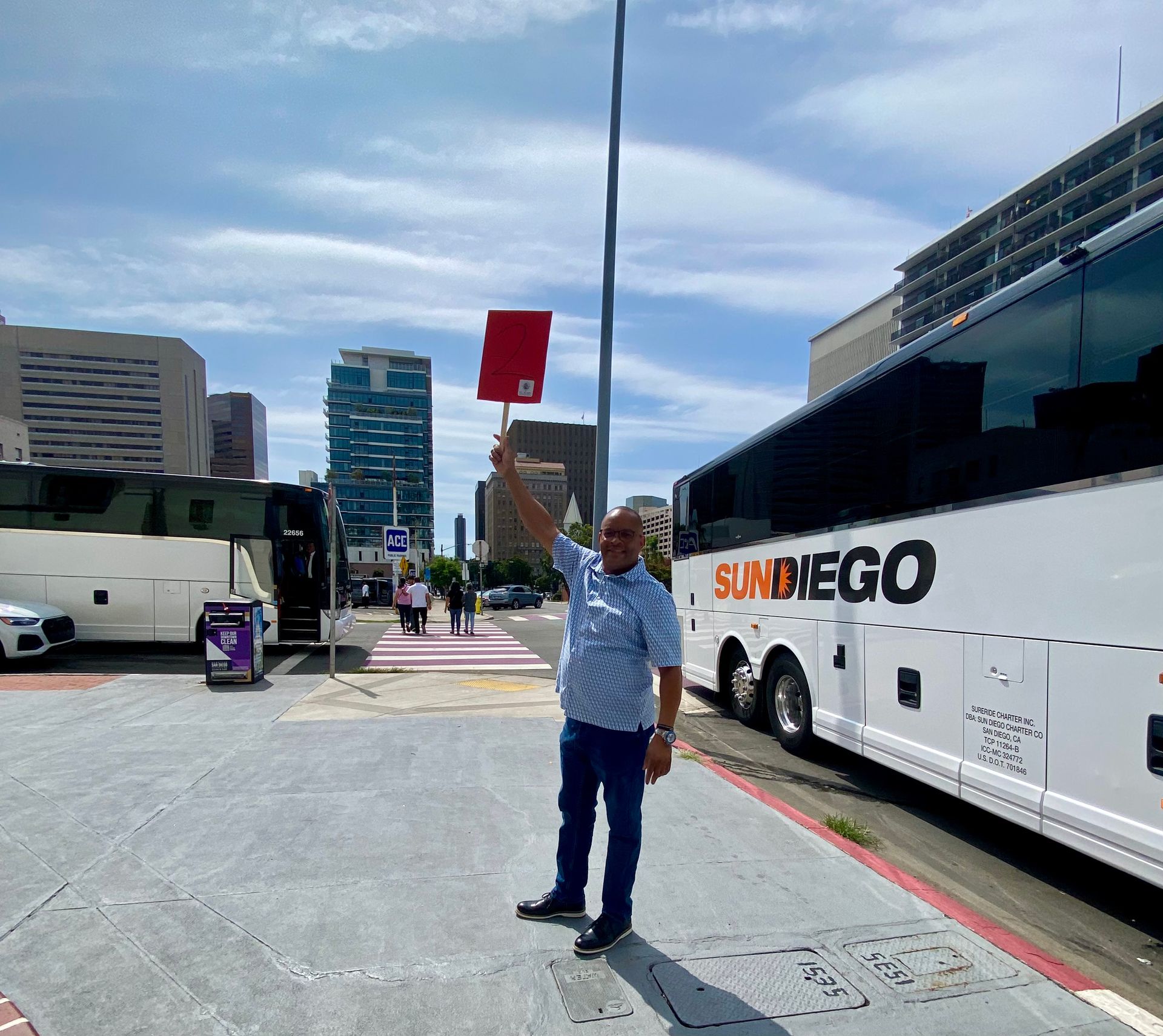 Man holding a red sign beside parked buses on a city street under a cloudy sky
