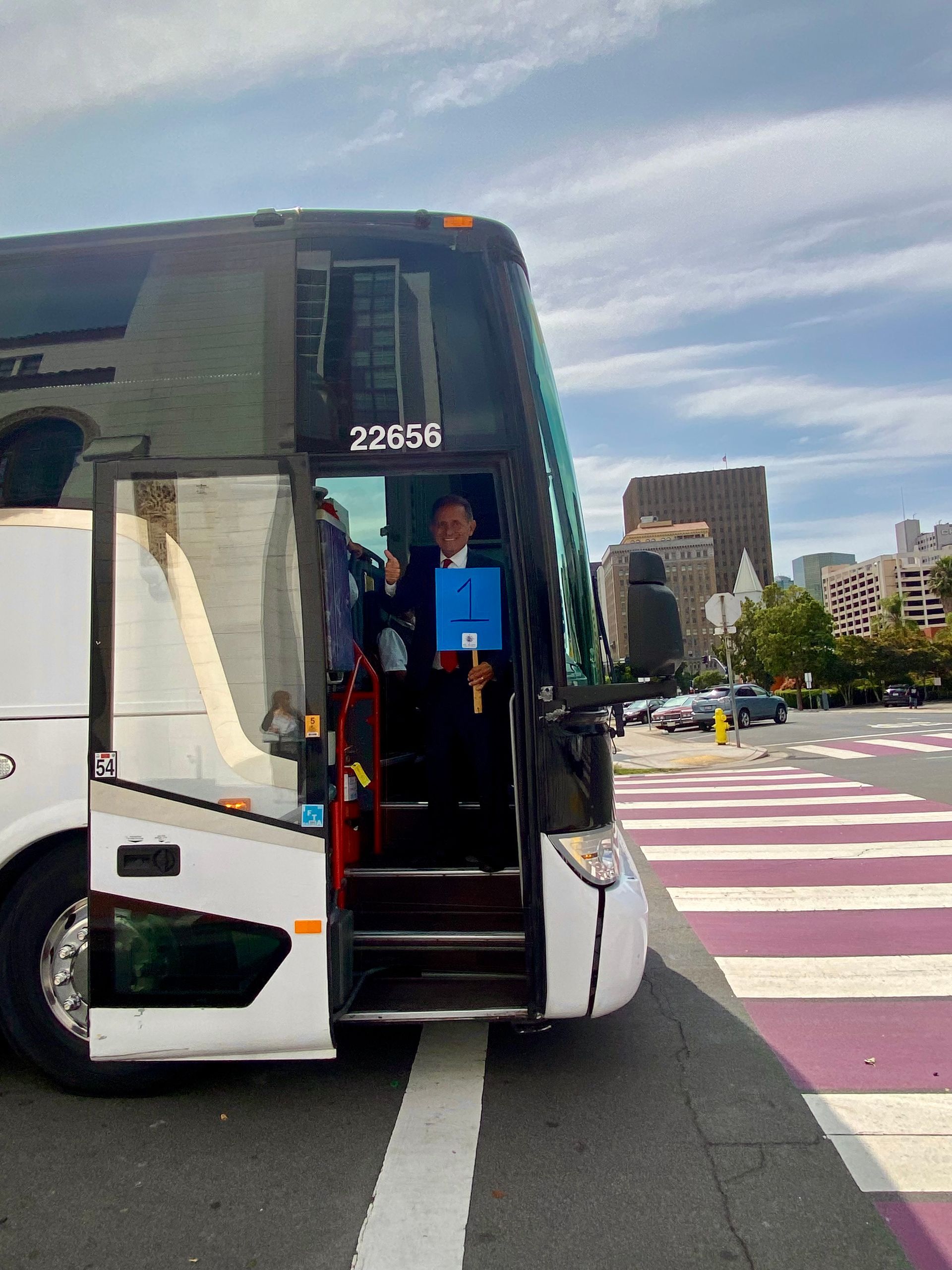Person stands in the doorway of a white bus on a city street near a crosswalk.