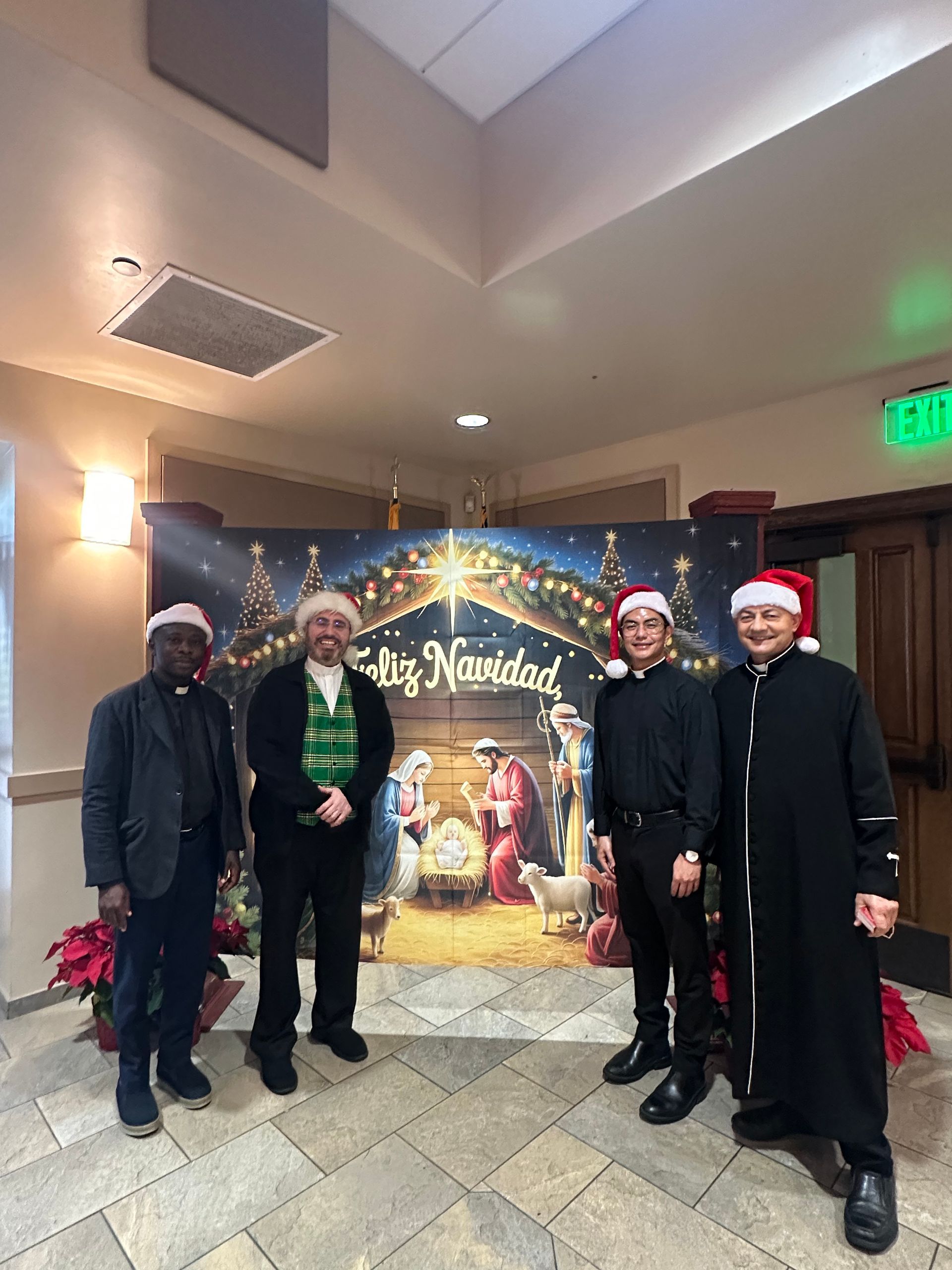 Four people in Santa hats posing in front of a festive holiday display indoors.