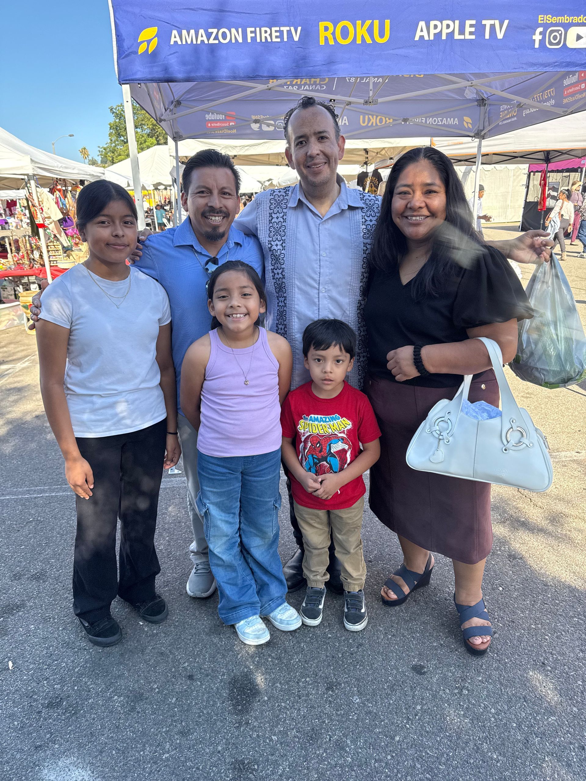 Family of five posing outdoors under a purple event tent, smiling beside sponsor banners.