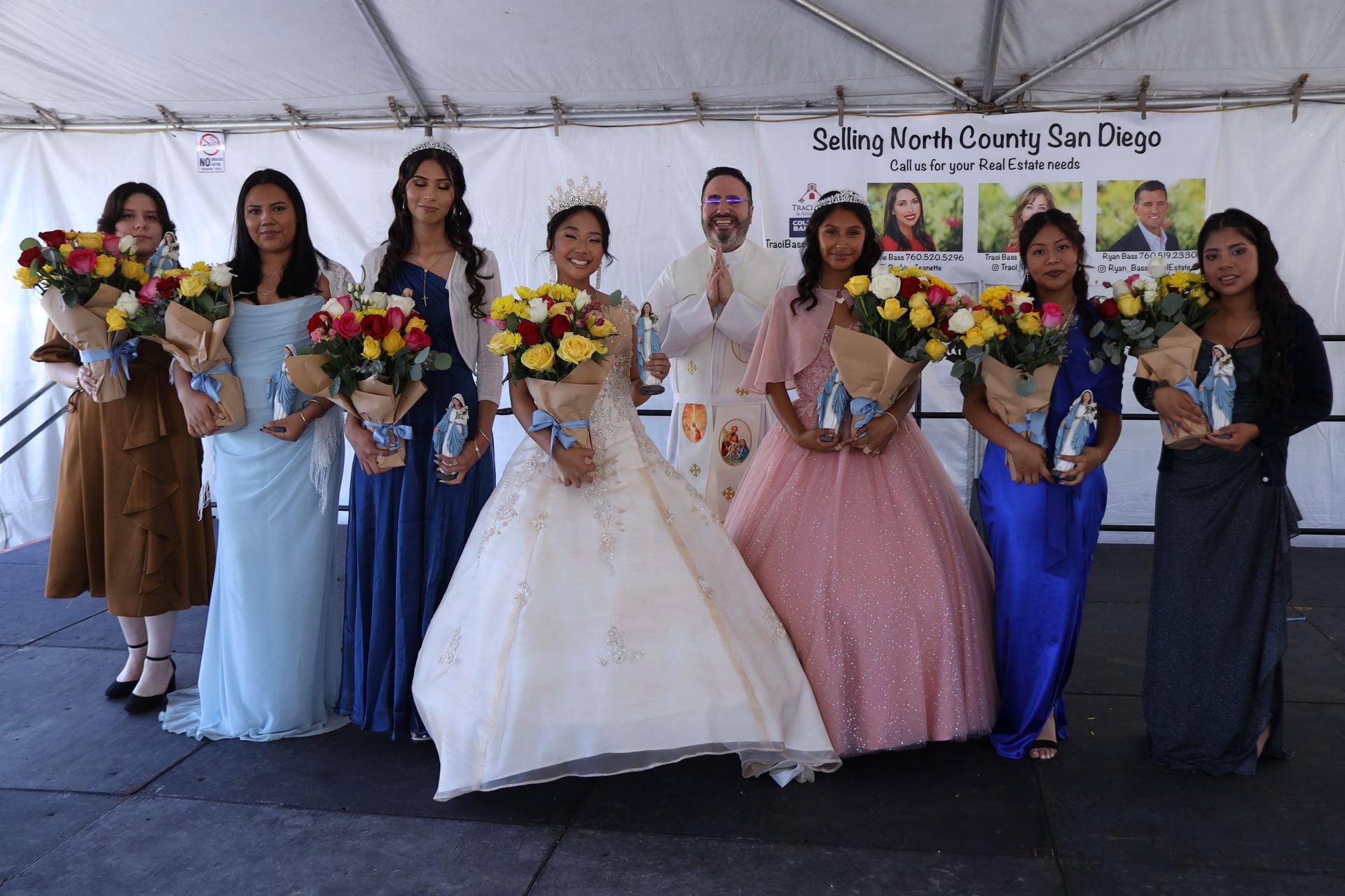 Award winners posing on stage with flower bouquets in formal dresses and suits