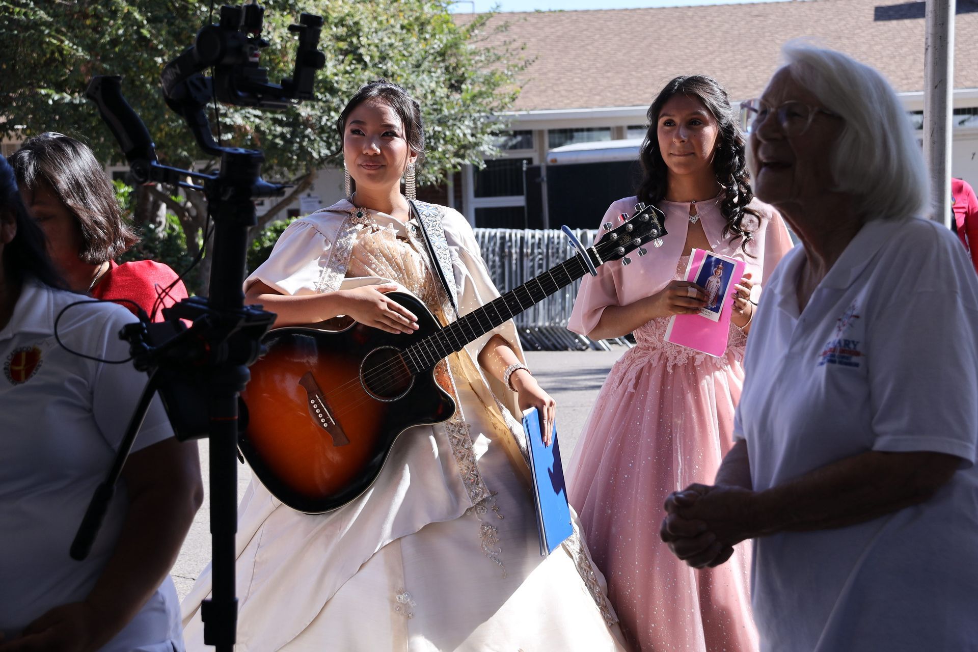 People outdoors with guitars and a pink dress, gathered in bright daylight.