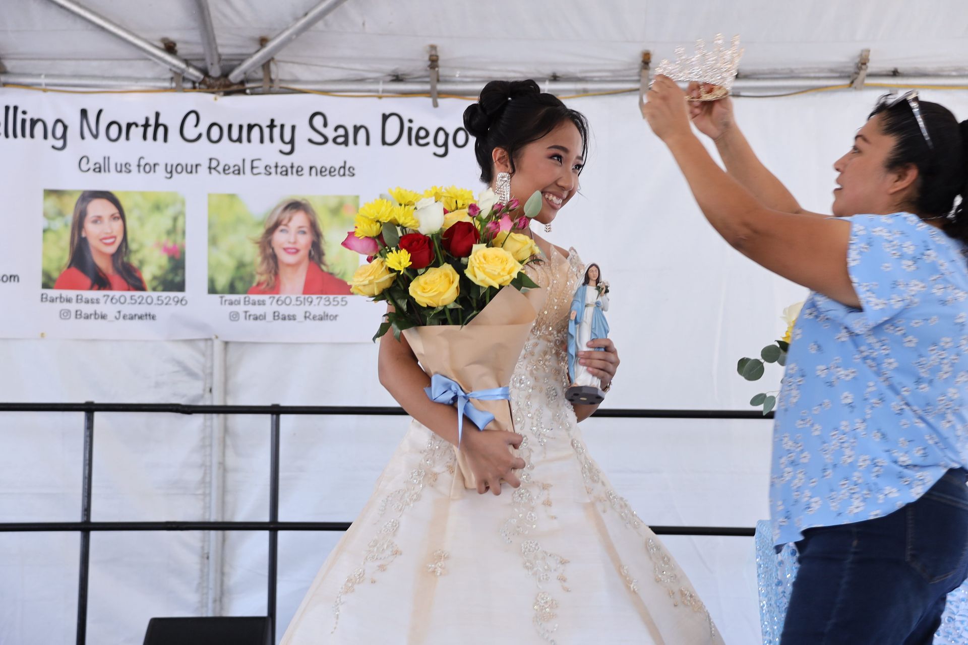 Bride with bouquet and woman in blue dress smiling on stage at an event