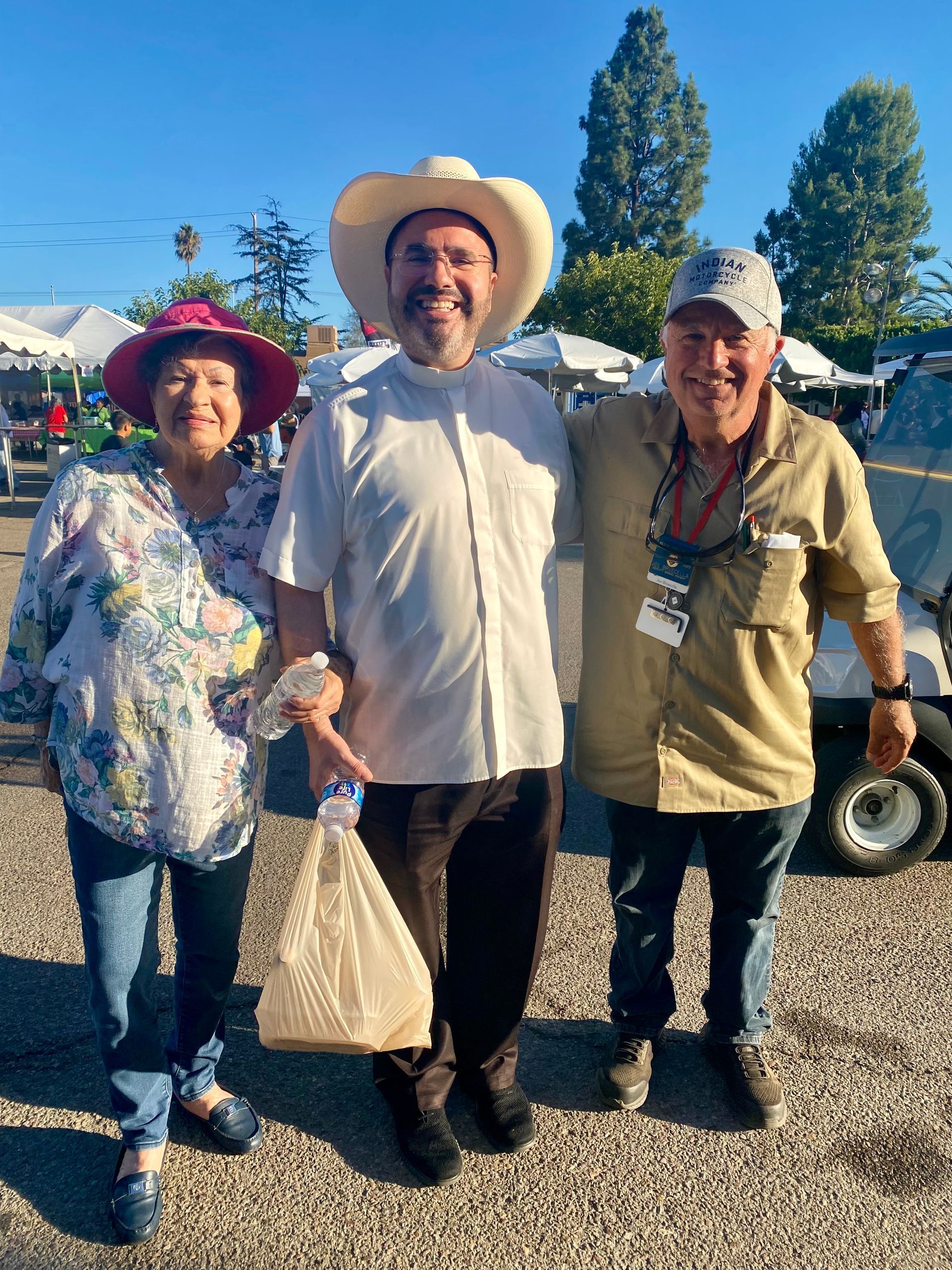 Three smiling people in cowboy hats standing together outdoors at a fair