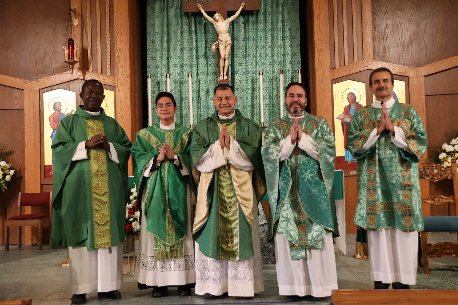 Five priests in green vestments stand in a church before an altar and crucifix, holding up chalices.