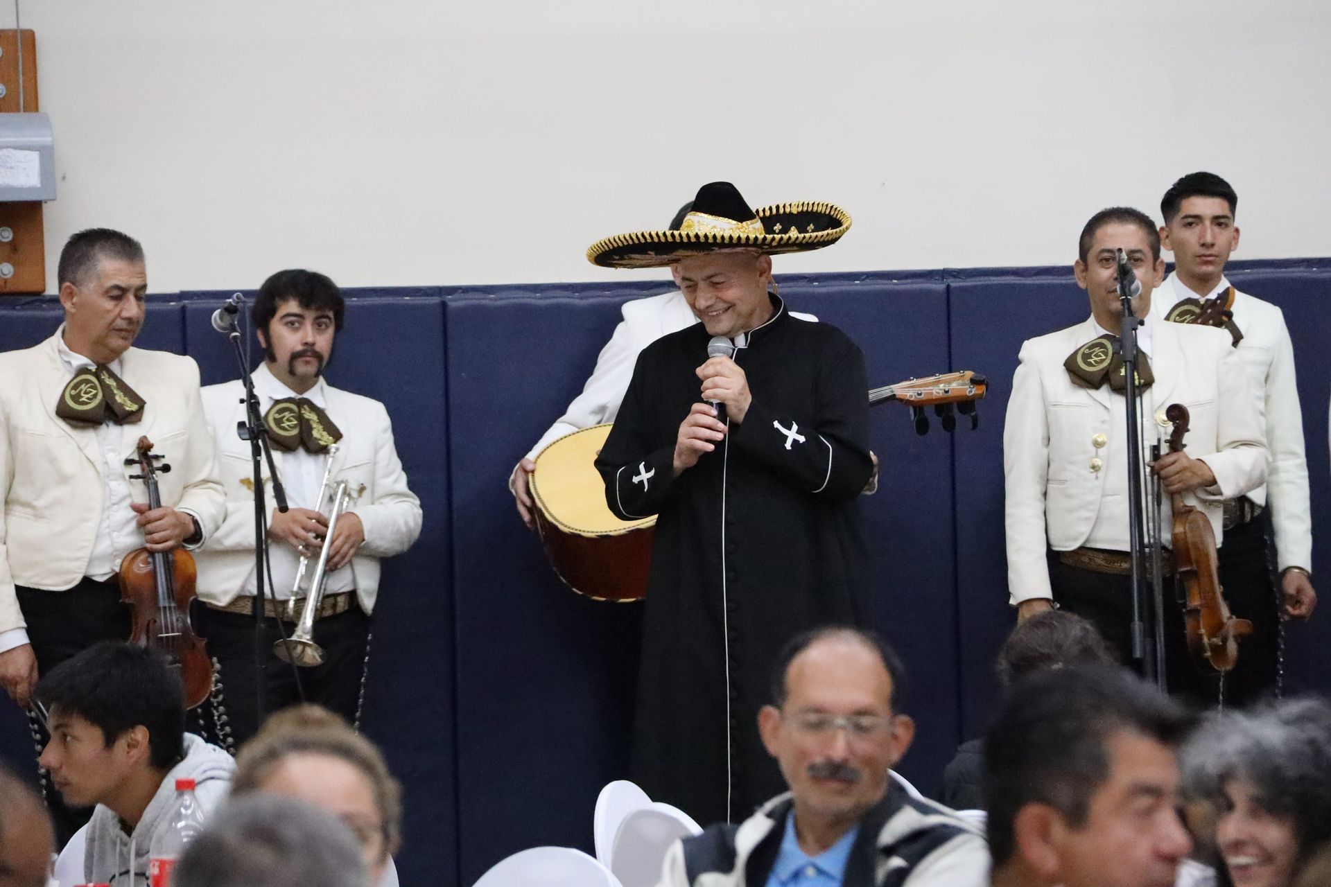 Mariachi band performing indoors, with a singer in a black sombrero at center stage