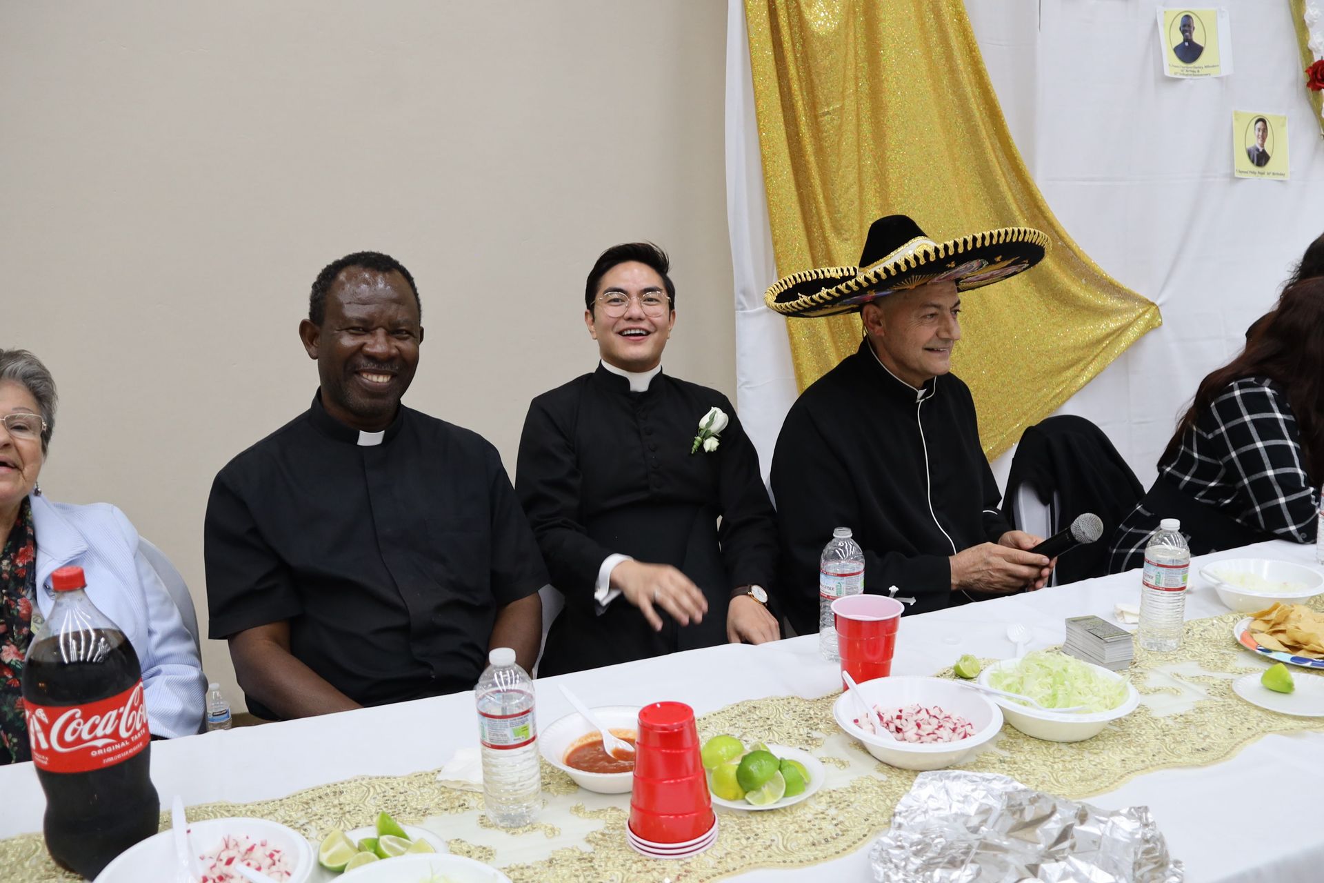People seated at a banquet table, wearing formal black attire and a sombrero, smiling at a decorated event.