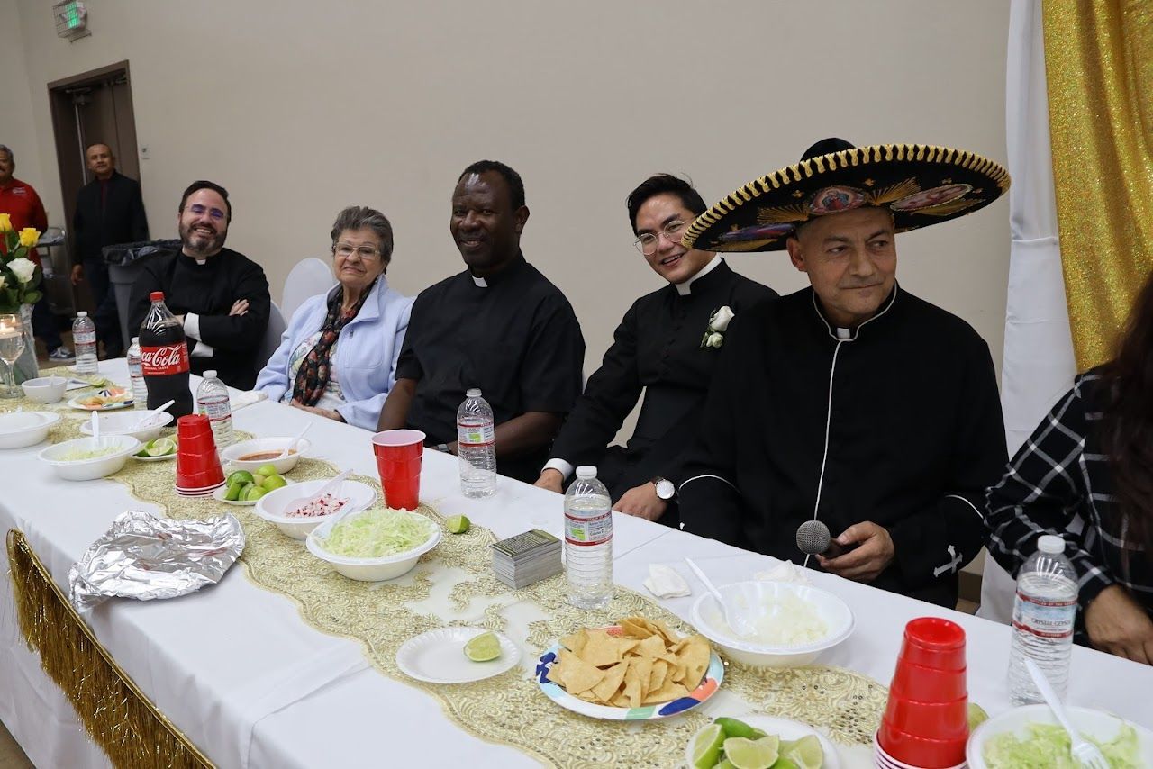People seated at a banquet table with food, drinks, and a man wearing a sombrero centerpiece