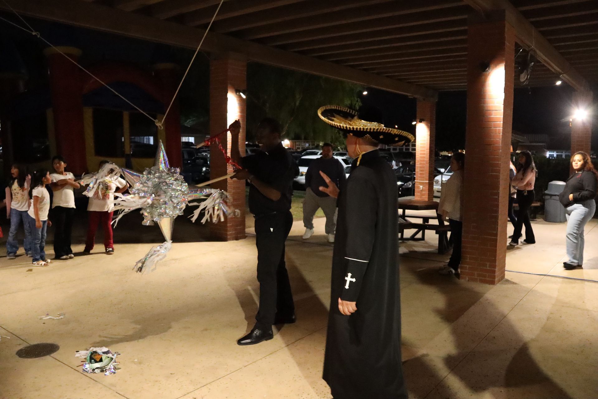 Costumed figures in black stand in an outdoor pavilion while people gather in the background.