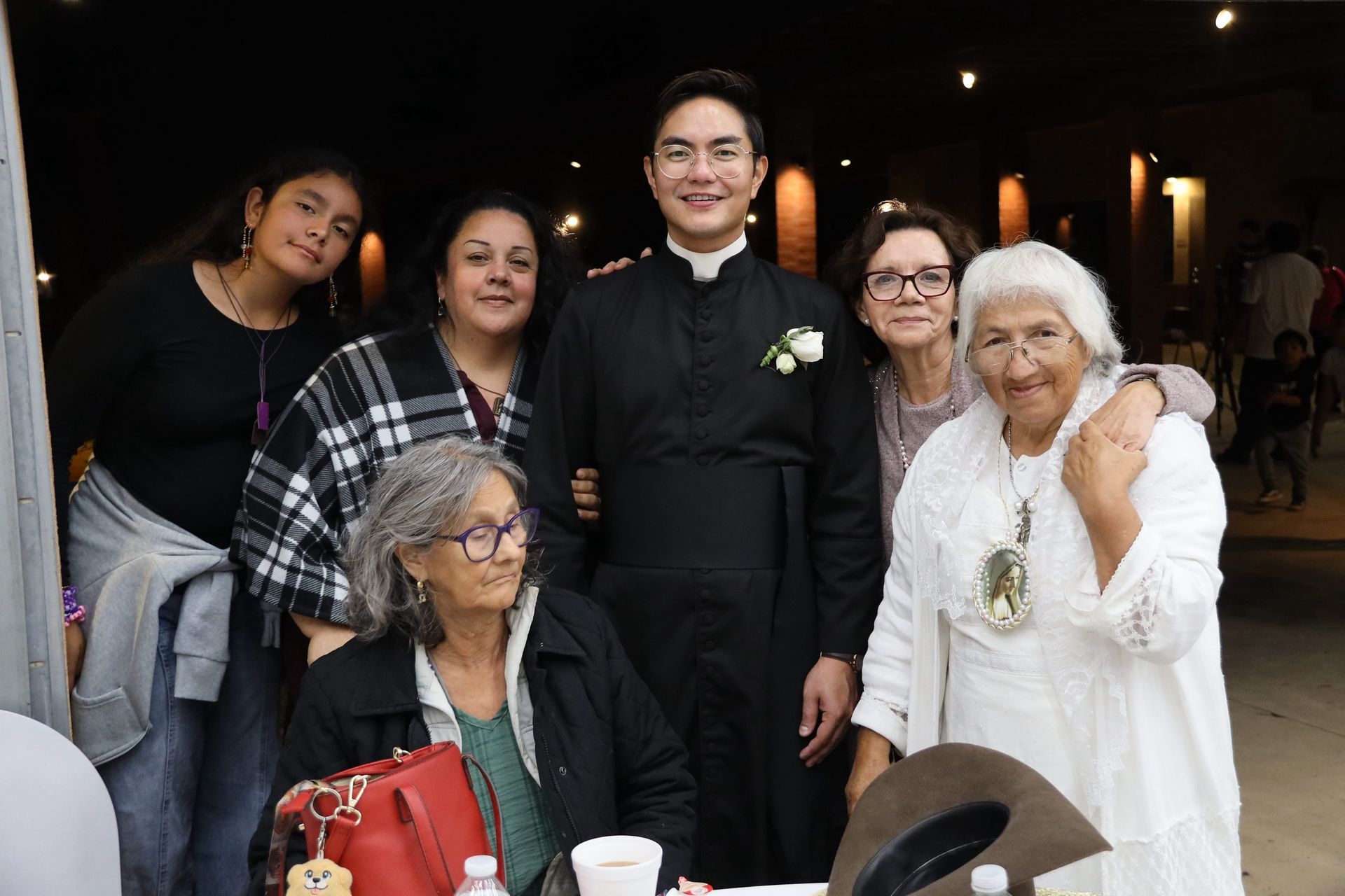 Group posing indoors at a celebration, with a man in black centered among seated and standing guests