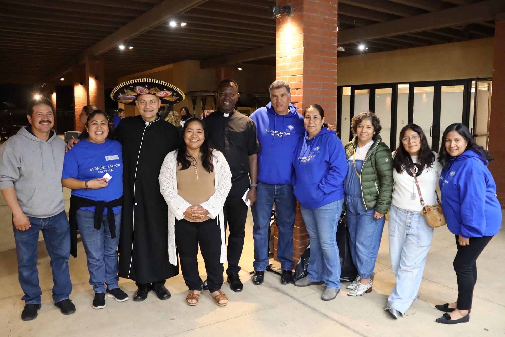 Group of nine people posing together indoors under a covered walkway, several wearing blue shirts.