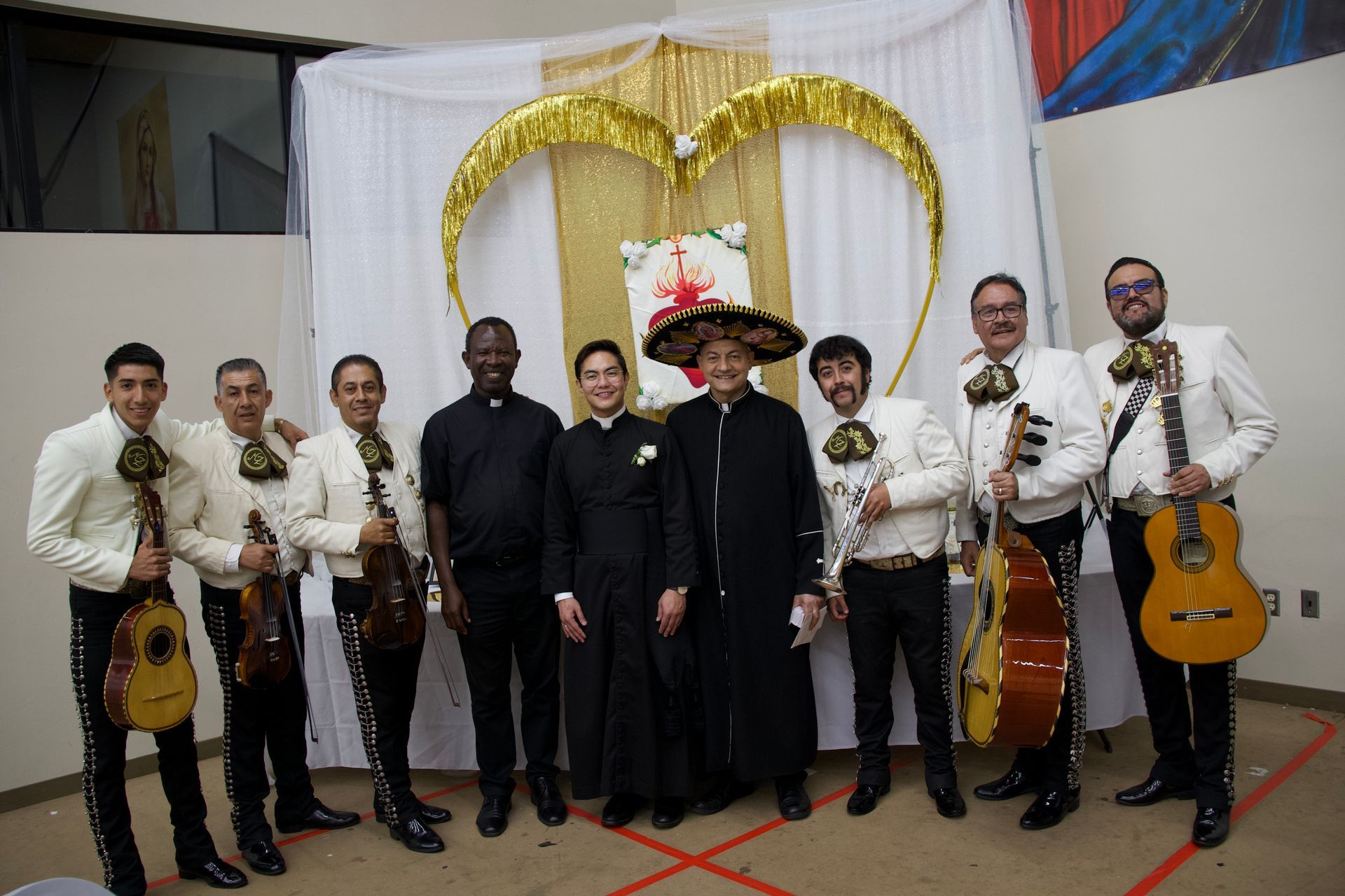 Formal group portrait of seven musicians in black suits holding violins, guitars, and trumpets before a gold backdrop