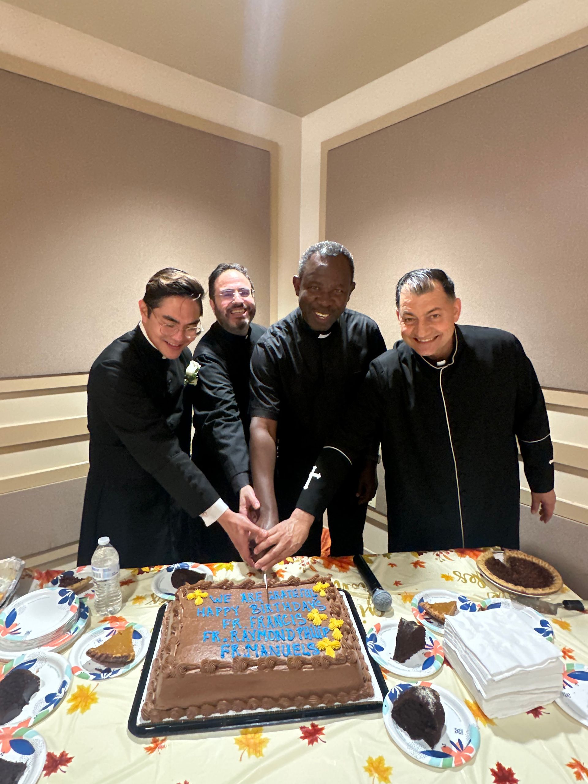 Four people cutting a chocolate sheet cake at a table with plates and desserts, smiling at a celebration