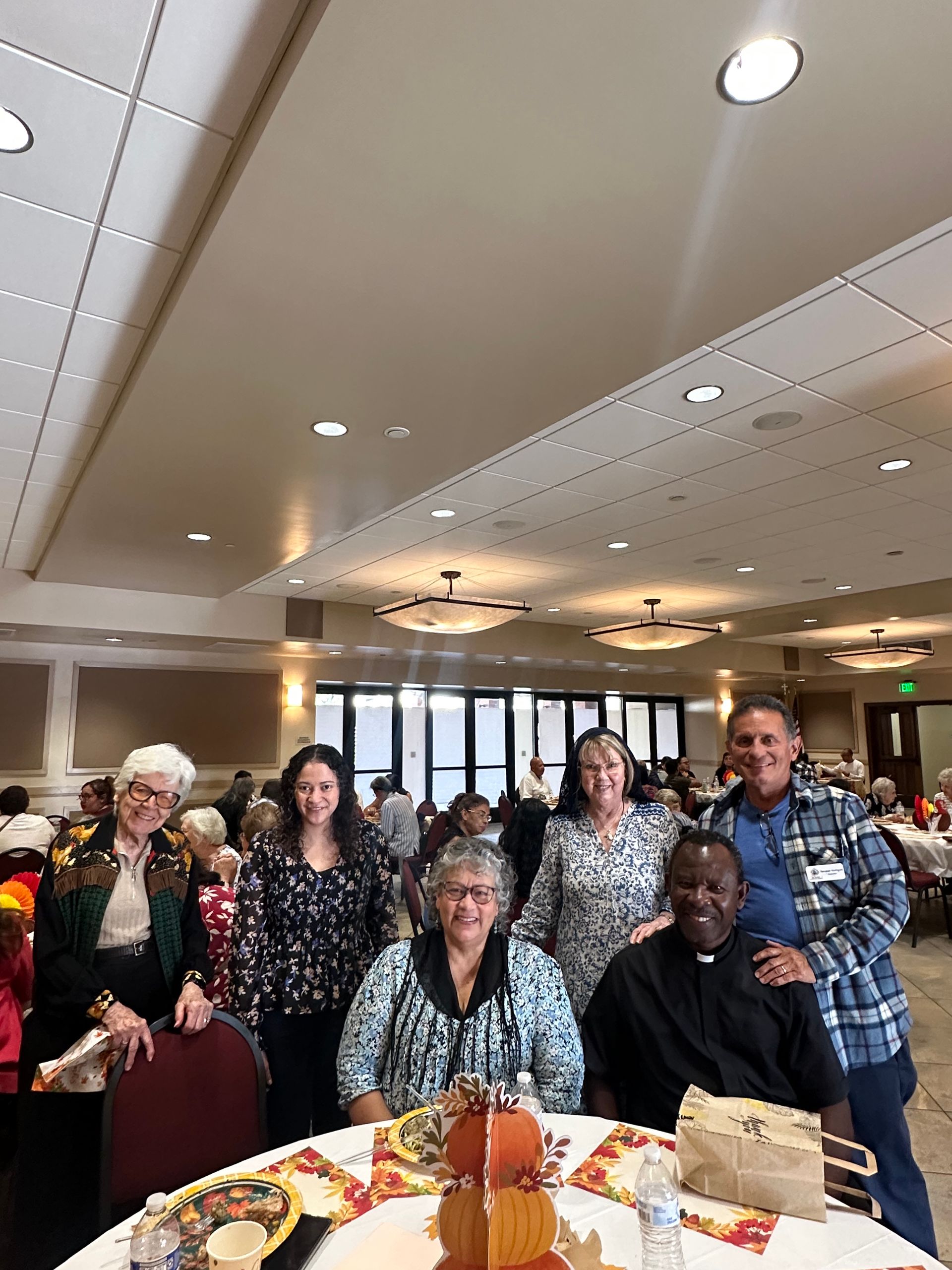 Group posing around a decorated table in a bright banquet room, smiling at a celebration event.
