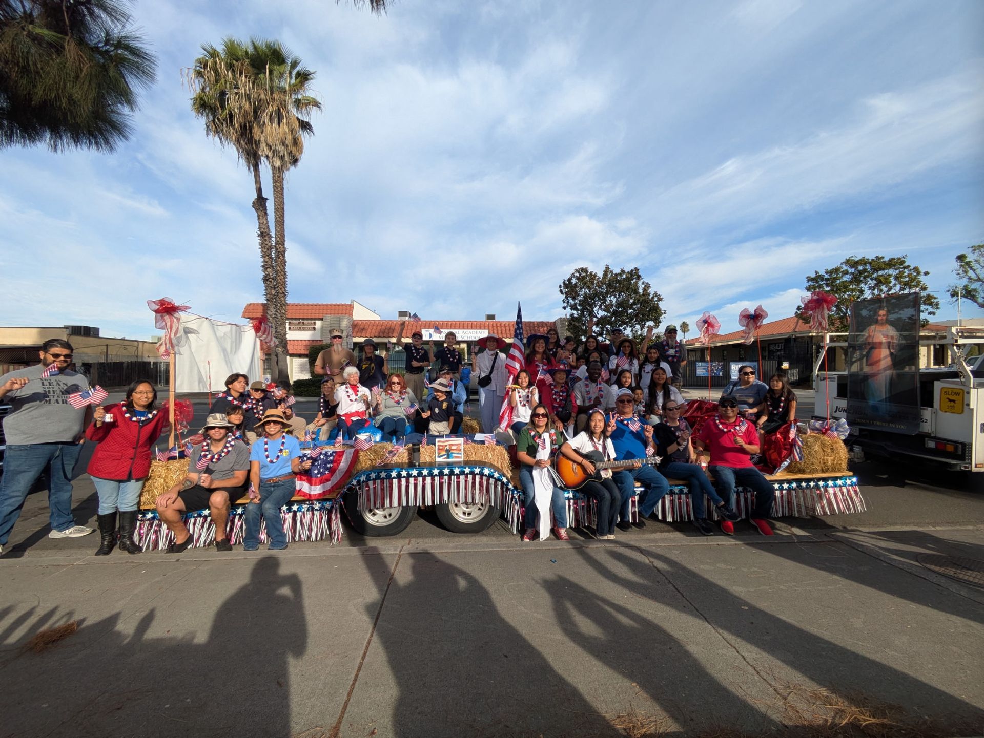 Large group posing outdoors with striped tablecloths, palm trees, and a clear blue sky.