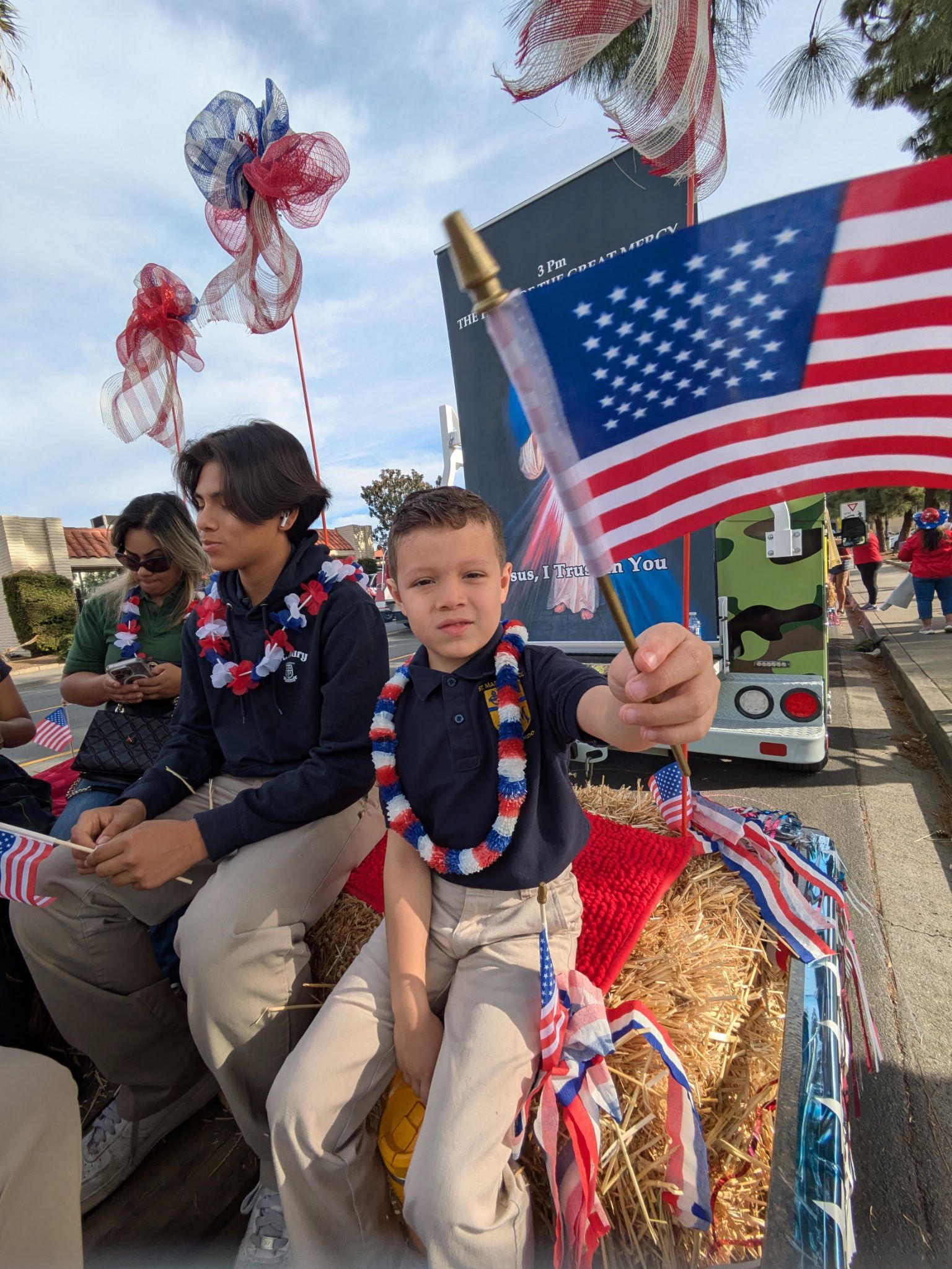 Child holding a small American flag in a parade float, with red, white, and blue decorations behind him.