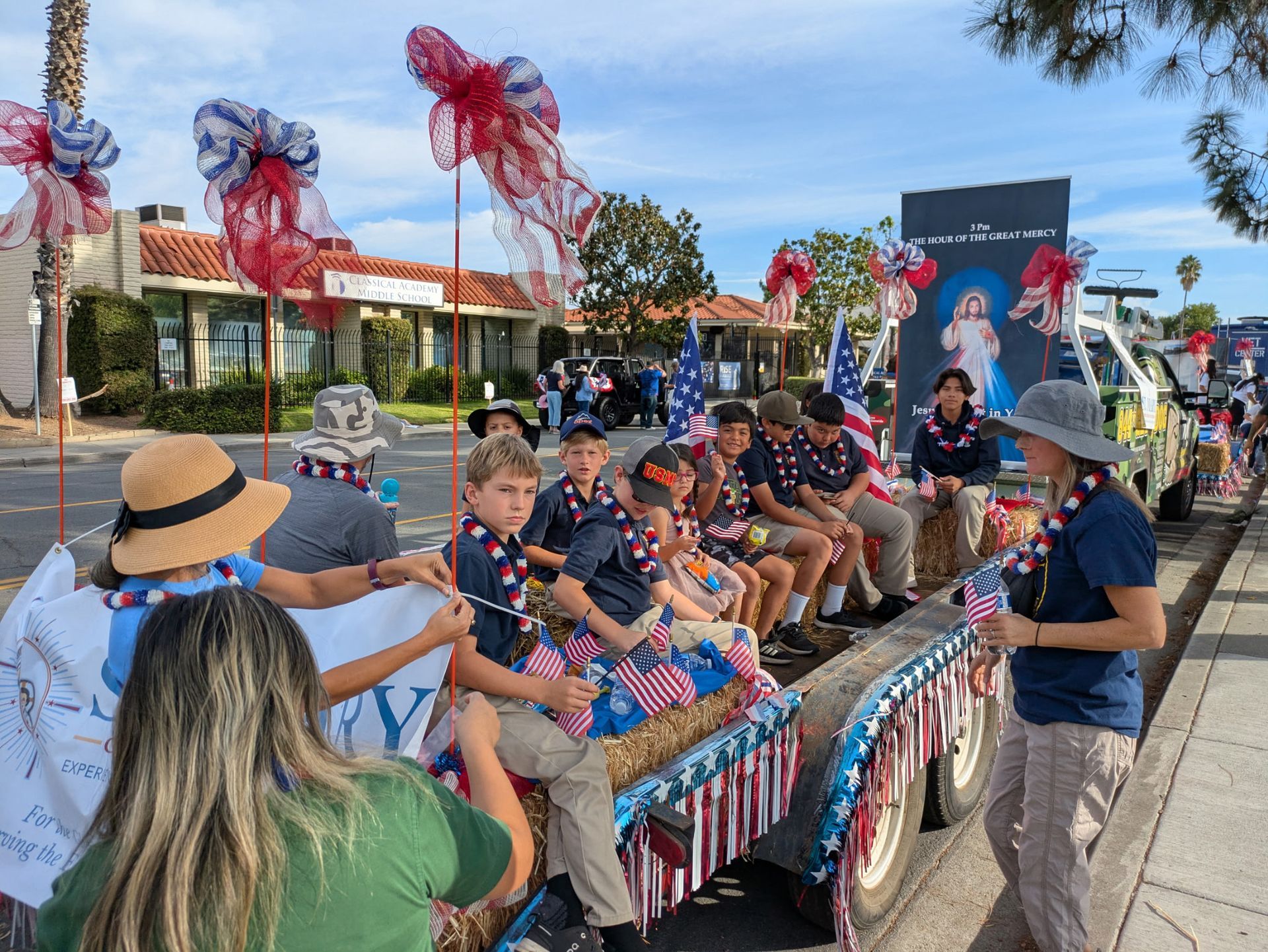 People on a decorated parade float wave red pinwheels on a sunny street.
