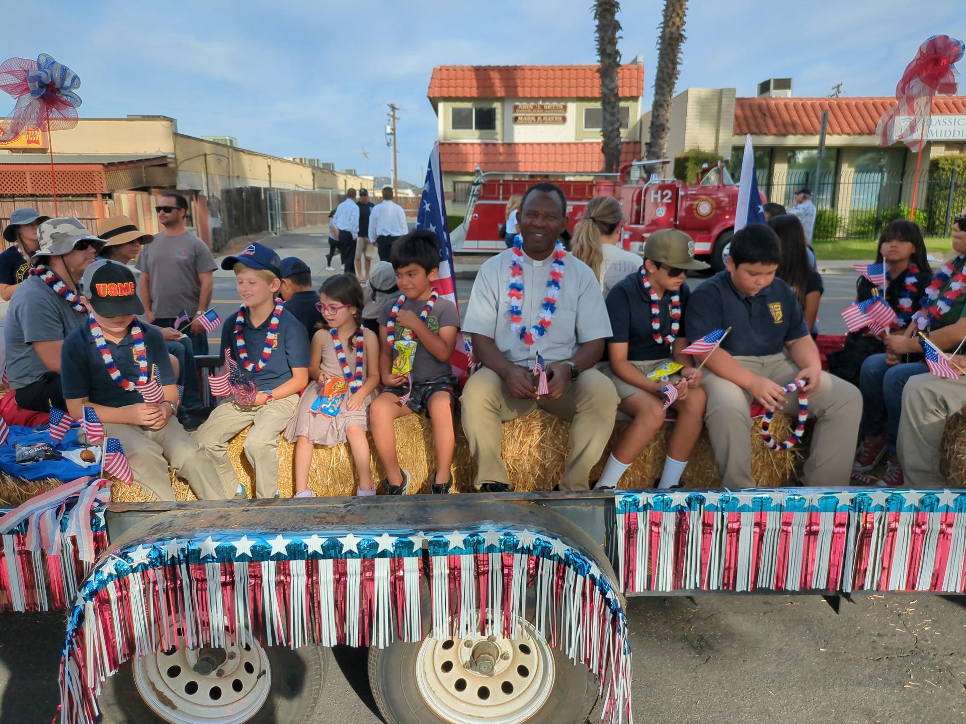 People seated on decorated float trailers during a festive parade on a street