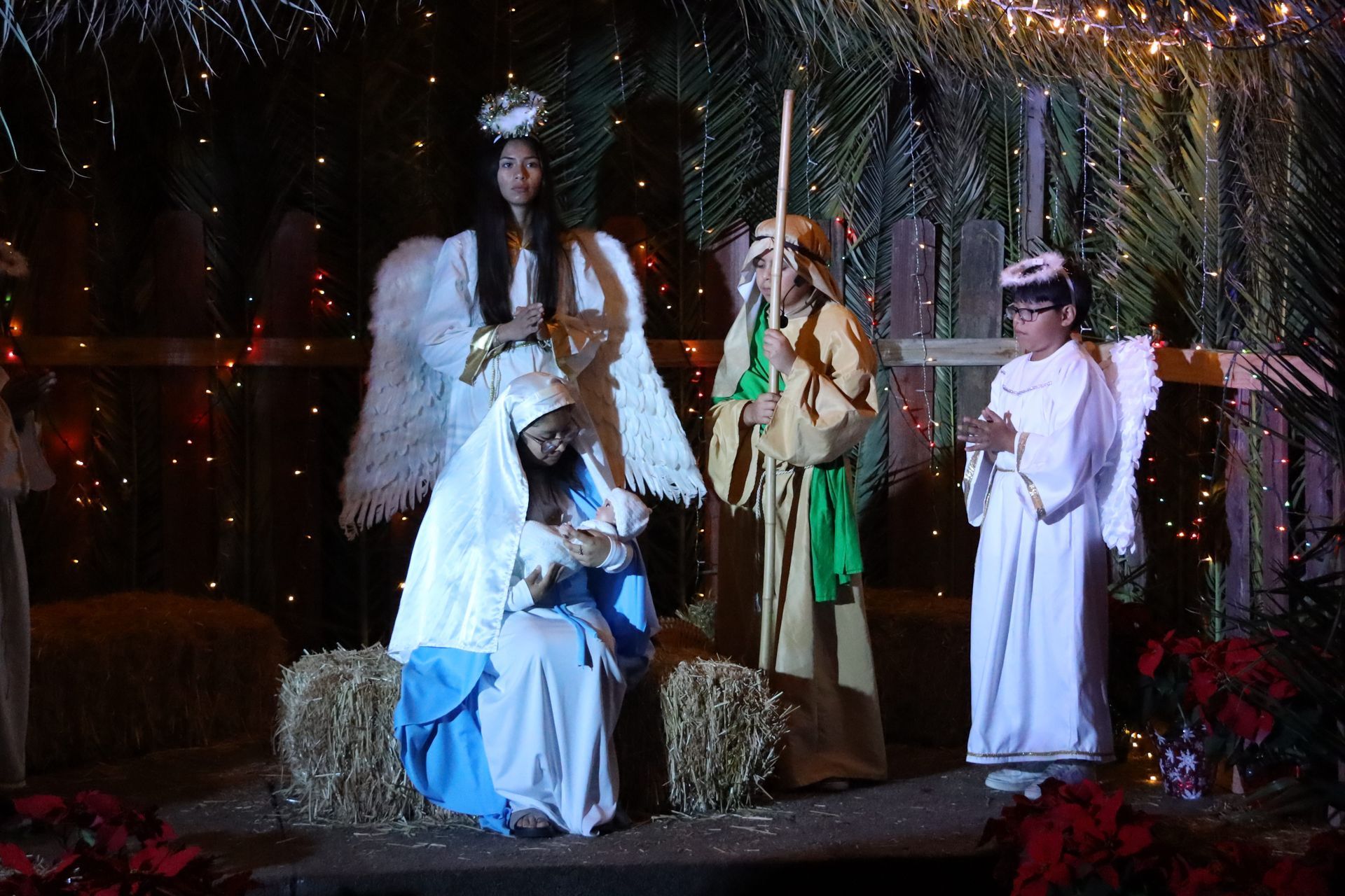 Nativity scene with figures of Mary, Joseph, and baby Jesus under festive lights