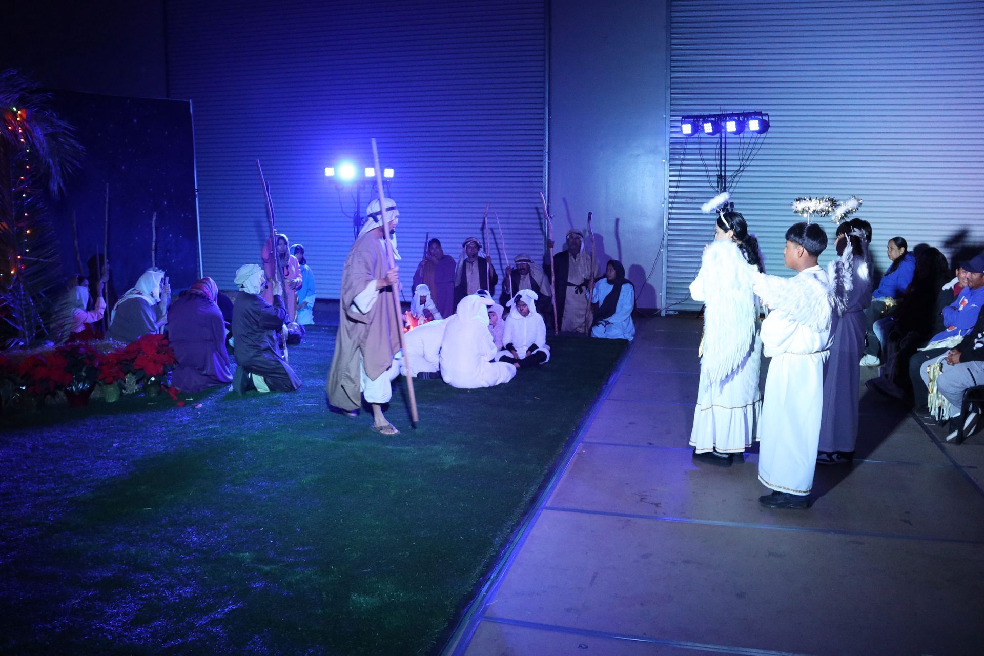 Nighttime outdoor performance with performers in white robes under blue lights near a building.