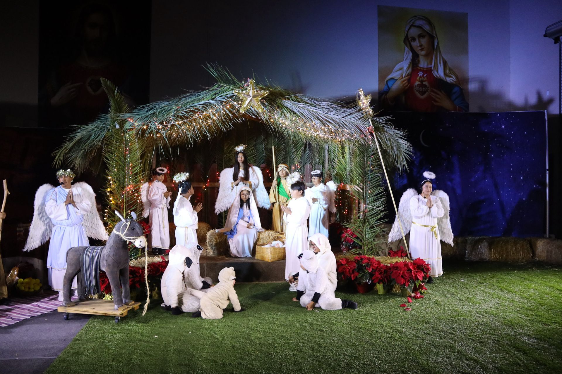 People in white costumes posing in front of a decorated nativity scene at night