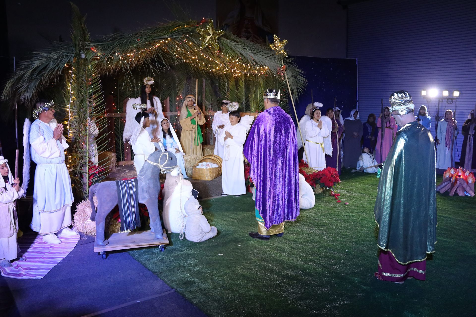 Costumed people on a lit outdoor stage at night, with a decorated gazebo and grass lawn